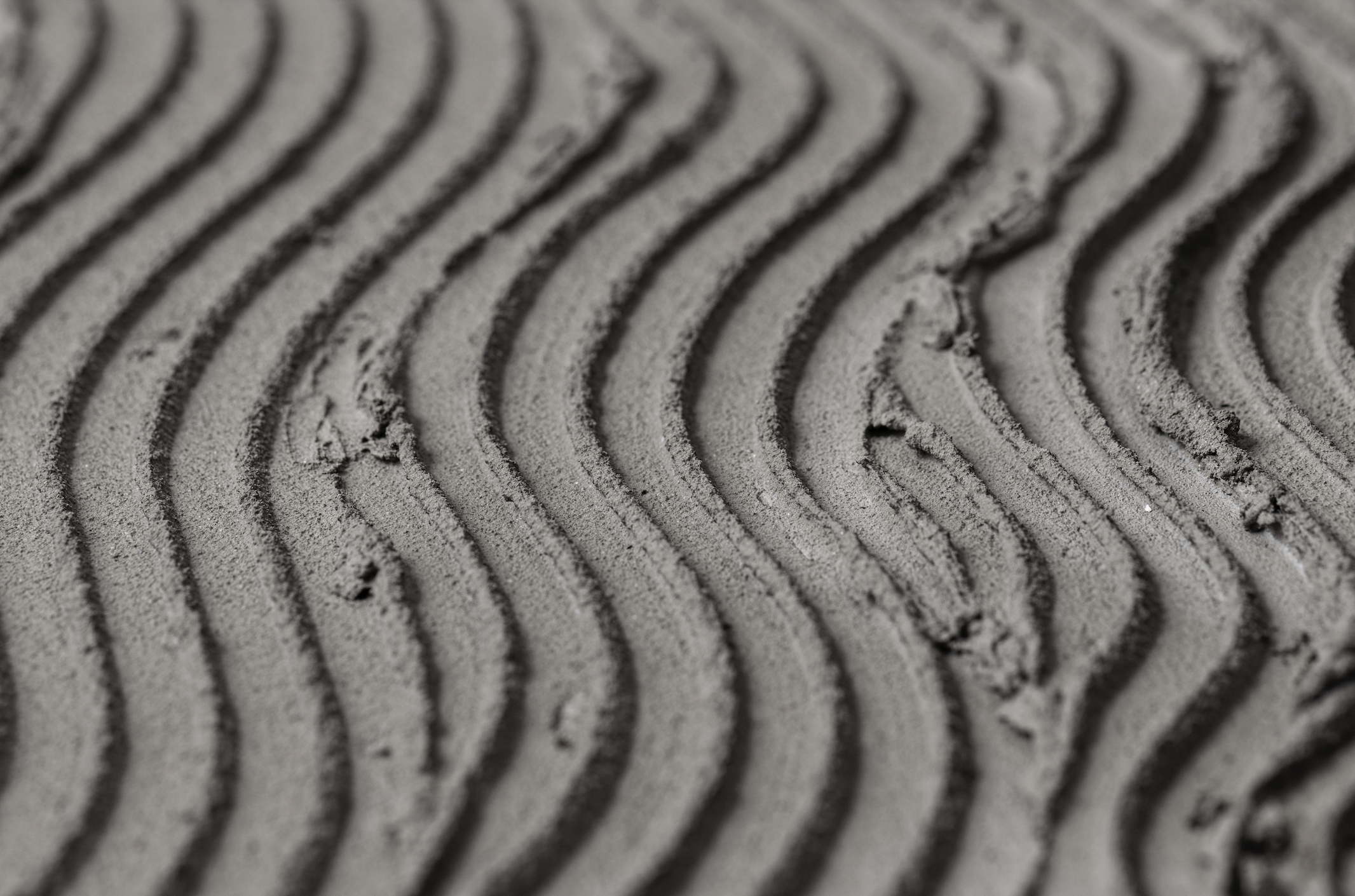 Close-up of textured sand with wavy, parallel ridges.