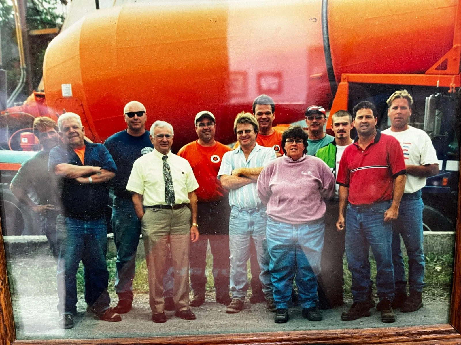 A group of men and women standing in front of an orange cement truck, posing for a photo outdoors.