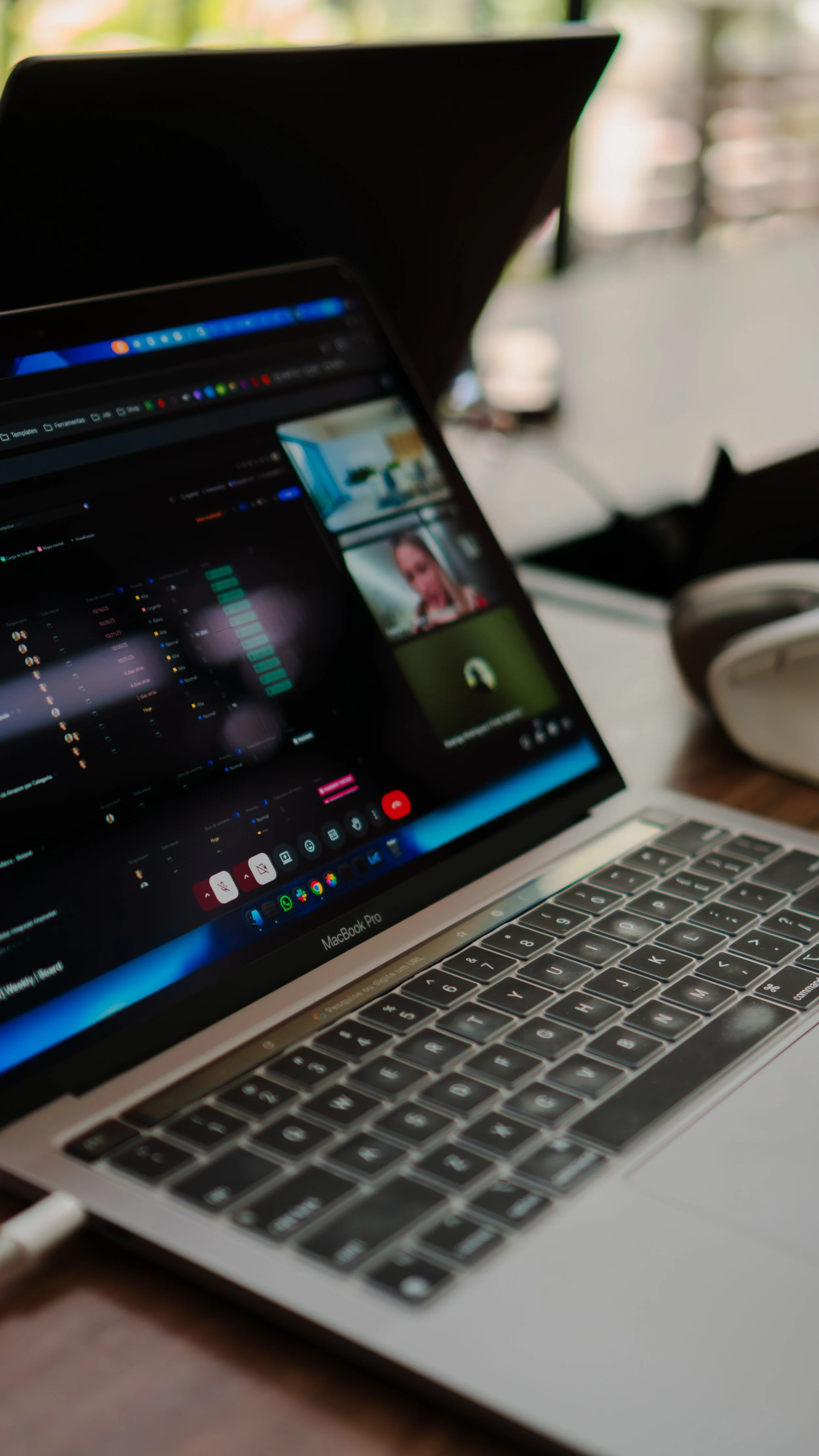 Close-up of a MacBook Pro laptop on a desk with an ongoing video conference, showing a woman speaking on the screen, and the laptop's keyboard in focus.