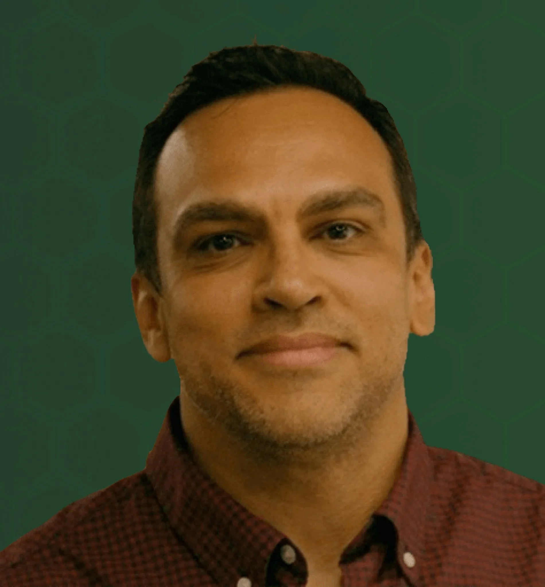 Close-up partial view of a person with dark hair, blue eyes, smiling, wearing a patterned shirt and a jacket, against a green background.