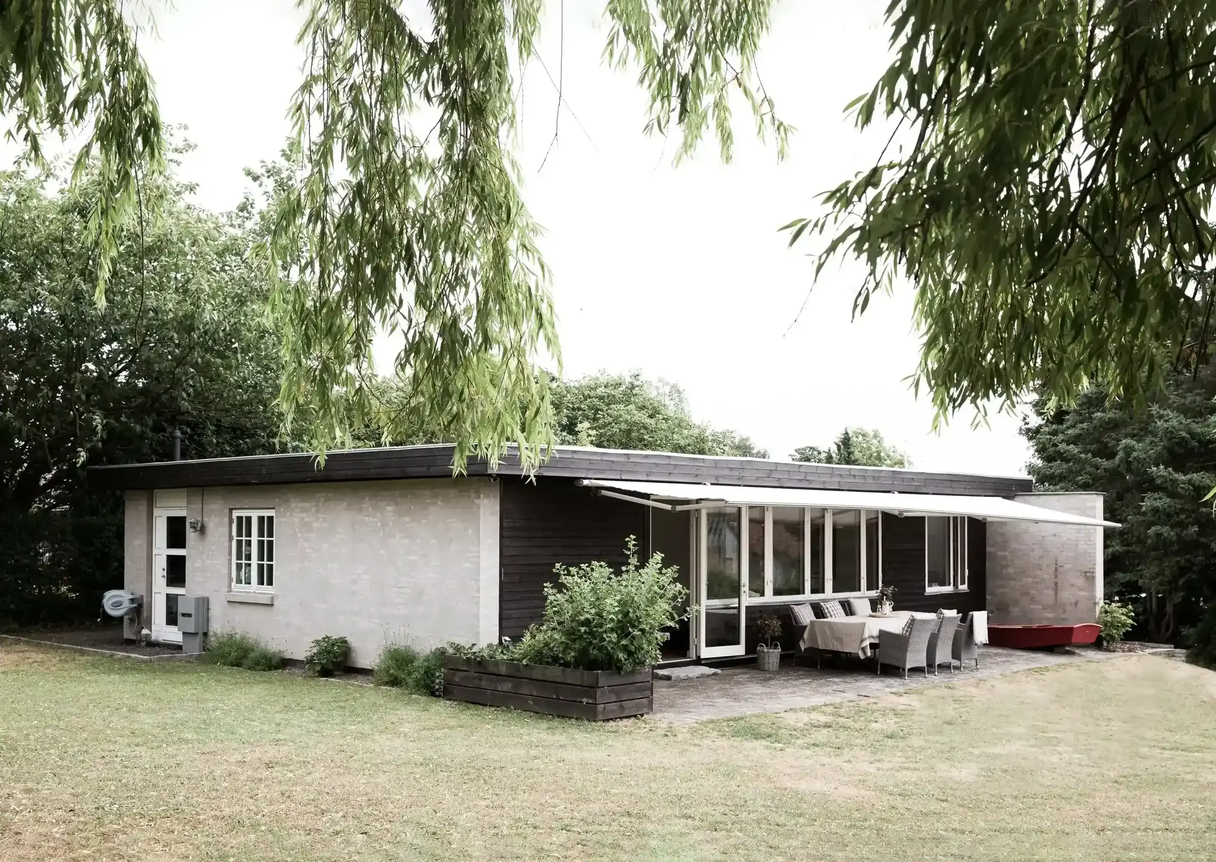 En moderne enkelt- eller fleretagers bolig med stort udendørs terrasse, omgivet af grønne træer og have.