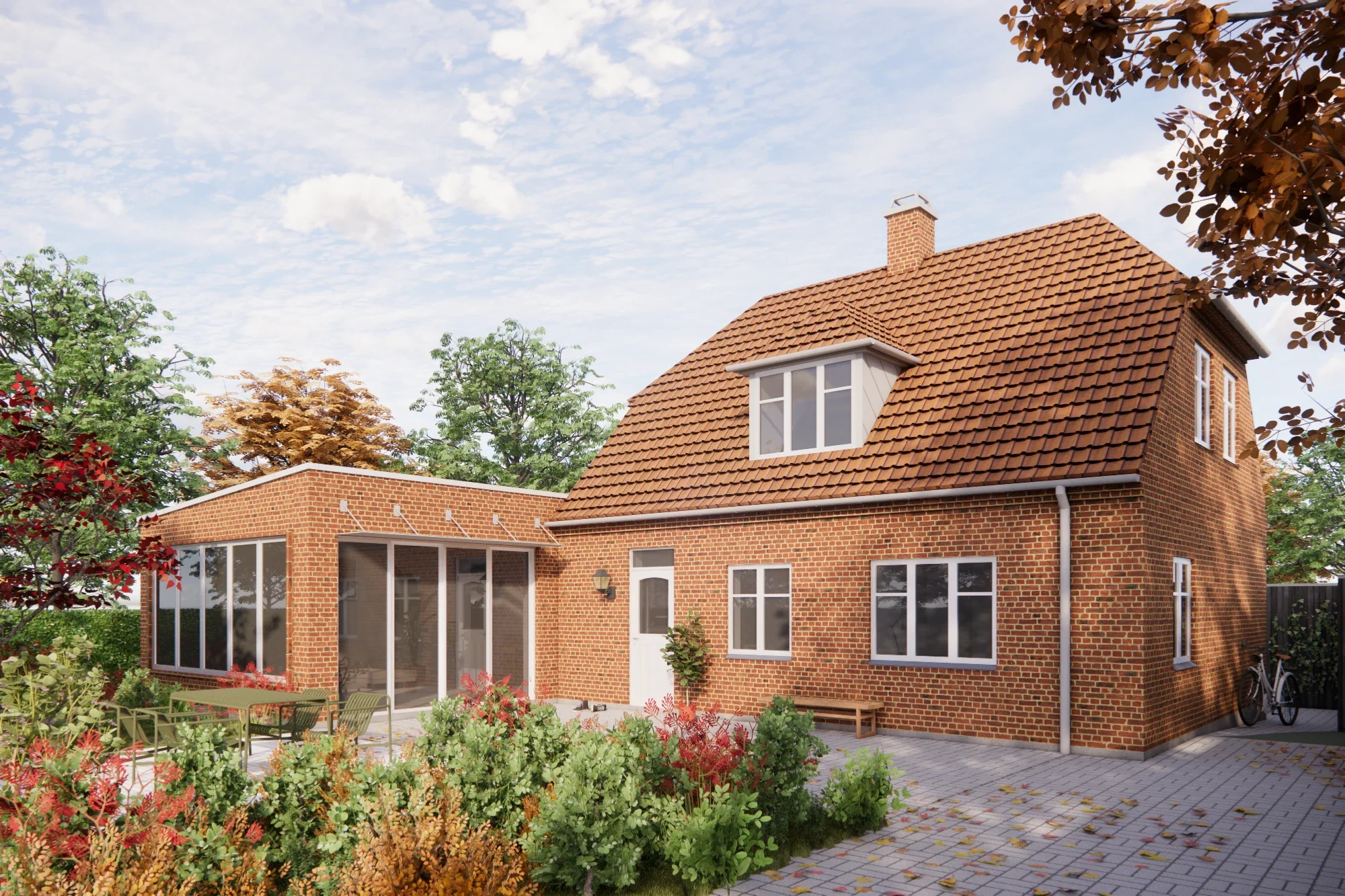 Et rødt murstenshus med sorte tage og store vinduer, omgivet af en have med buske, blomster og træer med efterårsblade, samt en udendørs terrasse med borde og stole.