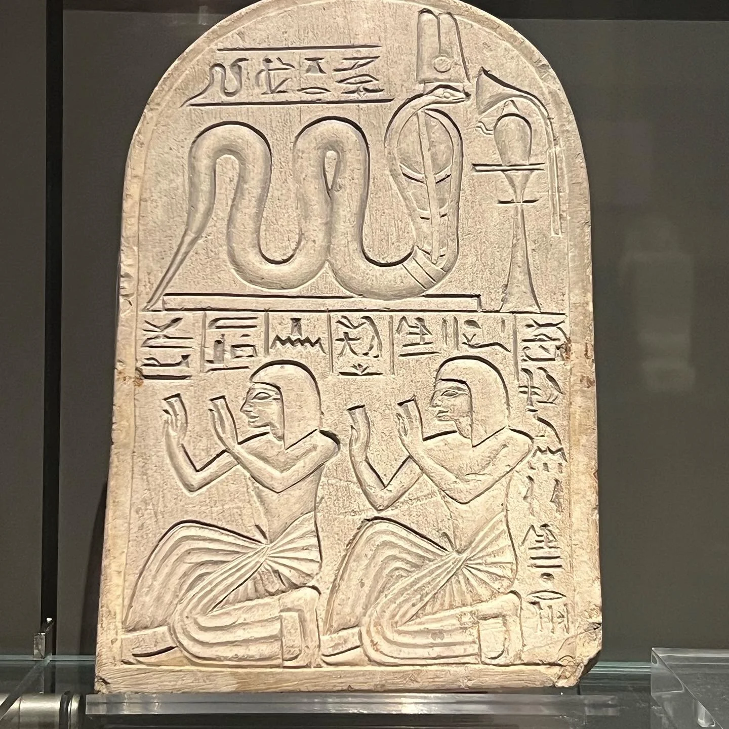 Ancient Egyptian carved stone tablet with hieroglyphics, two kneeling figures, and symbols of a snake and an ankh.