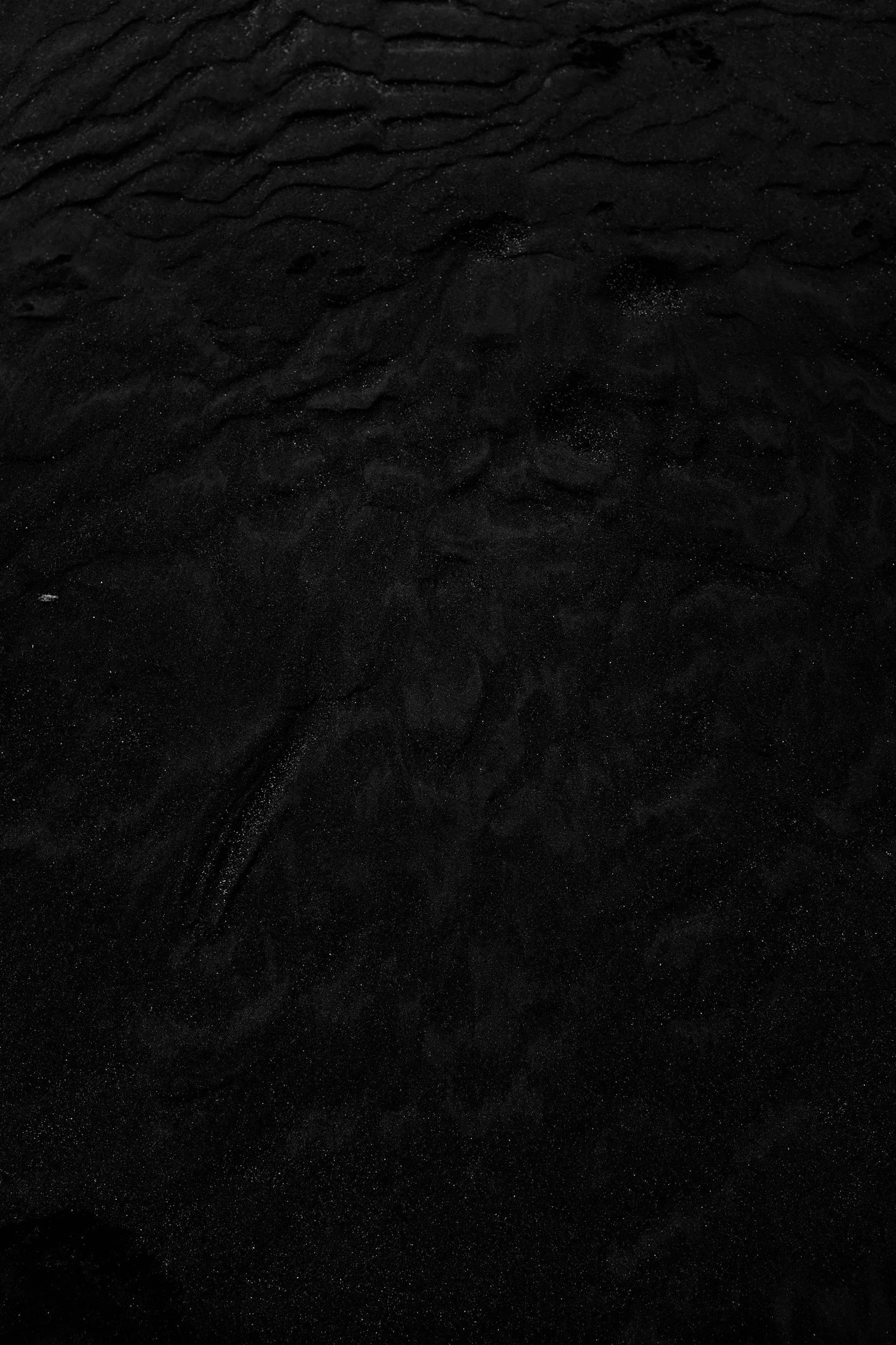 Close-up of dark sand with small white specks and textured ripples.