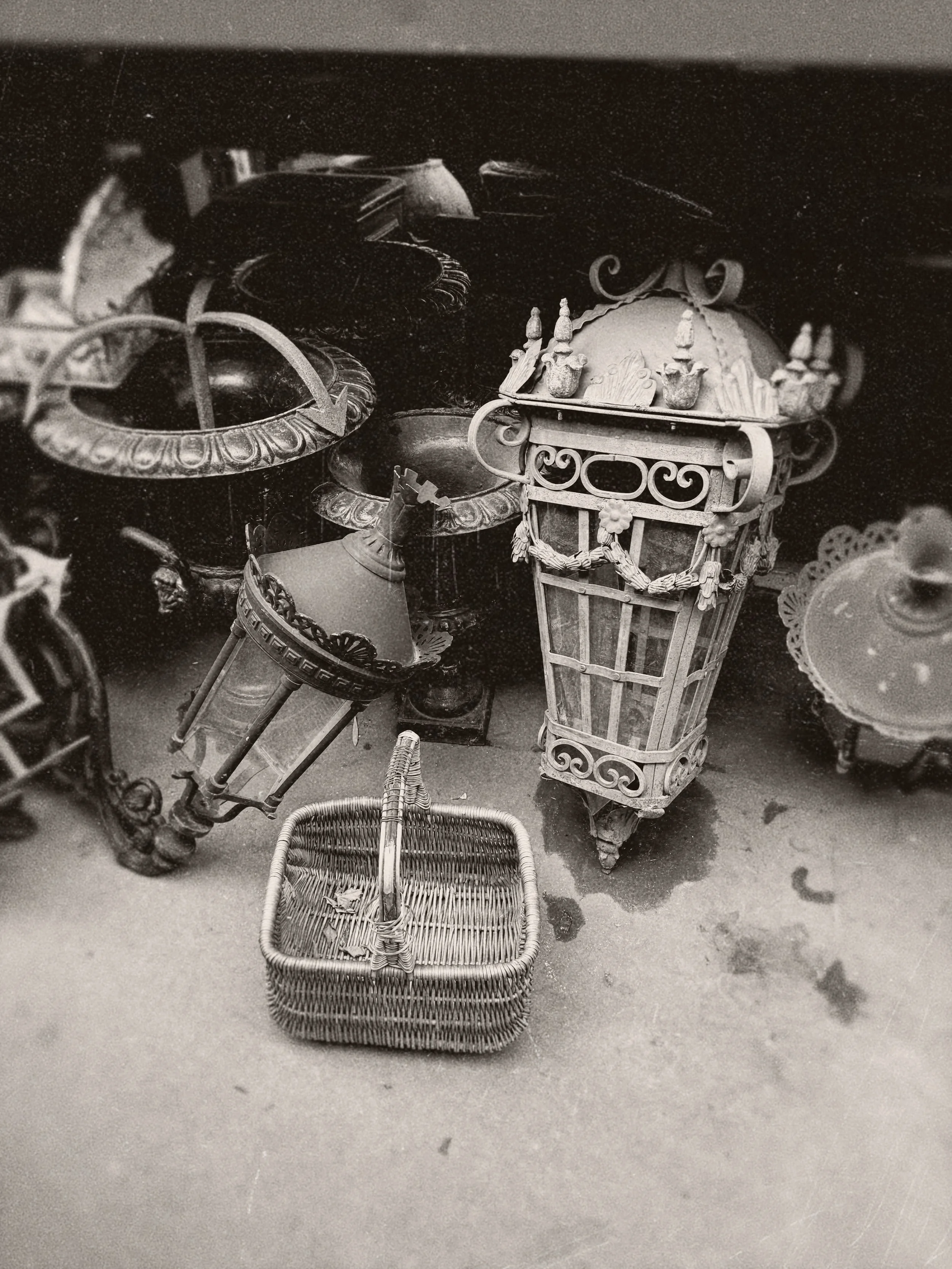 Black and white photo of vintage street lamps and a wicker basket on concrete ground.