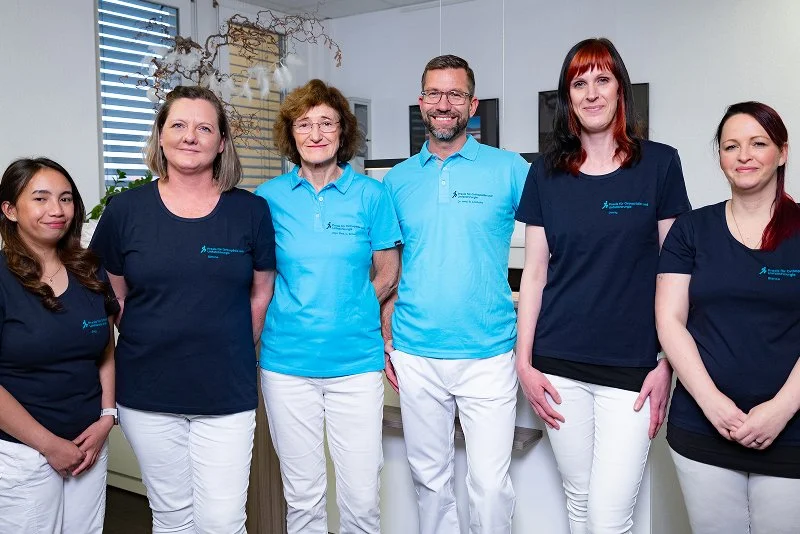 Sechs Personen in Berufskleidung, vor einem modernen Bürohintergrund, die gemeinsam für ein Foto posieren.