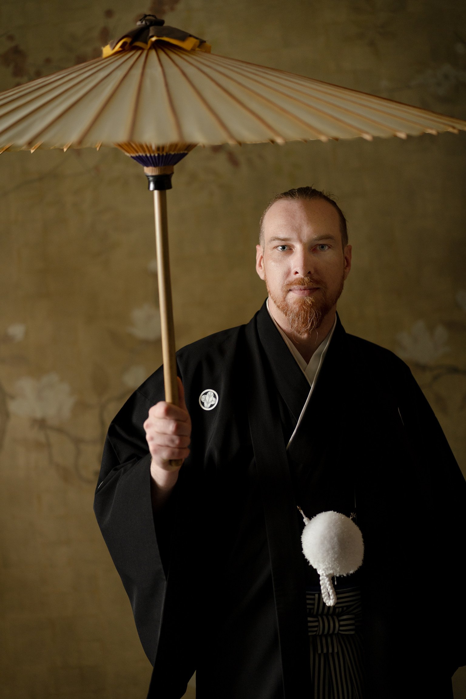 A man dressed in traditional Japanese attire holding a paper umbrella.
