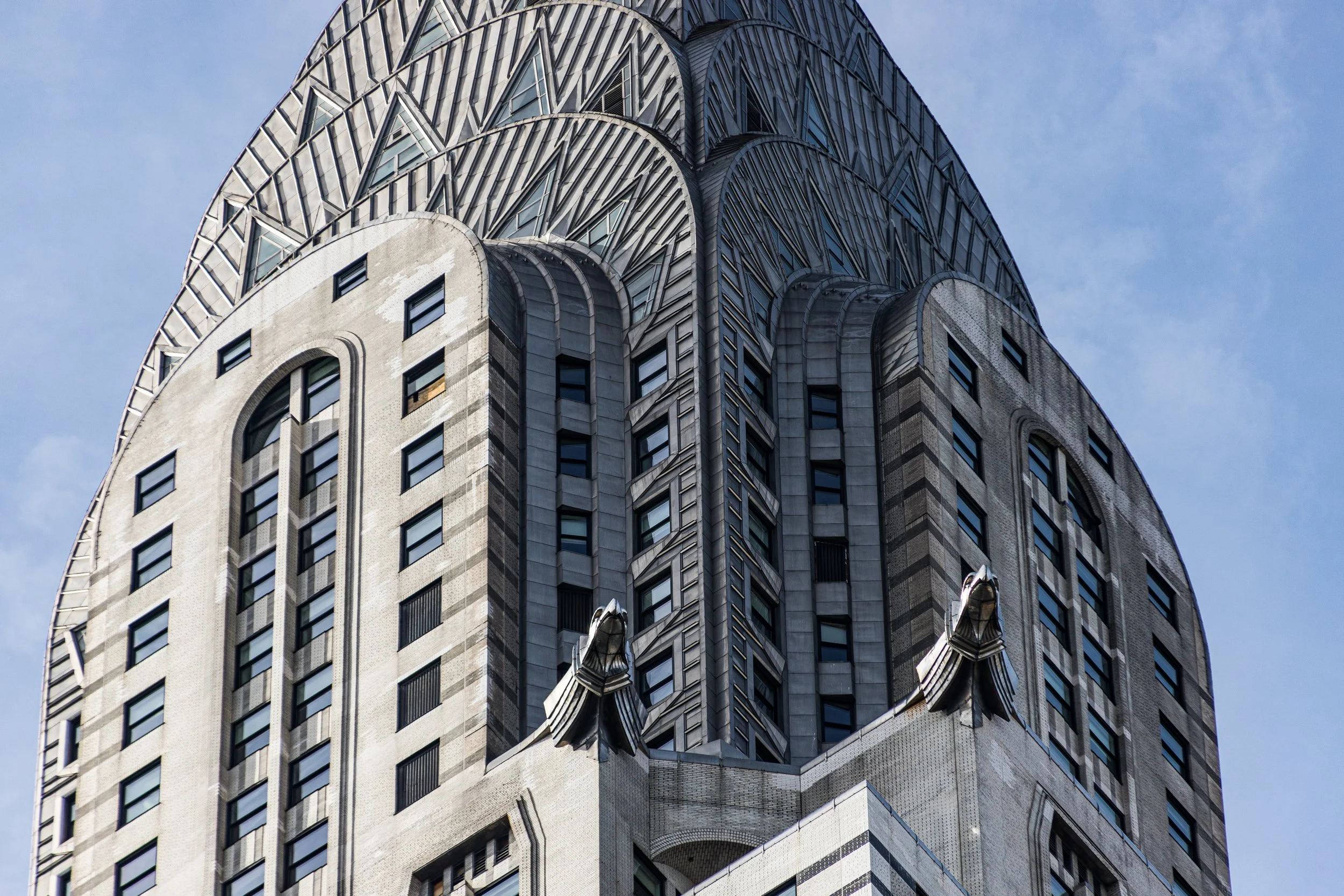 Close-up of the top portion of the Chrysler Building, an art deco skyscraper in New York City, showcasing its ornate spire and architectural details against a clear blue sky.