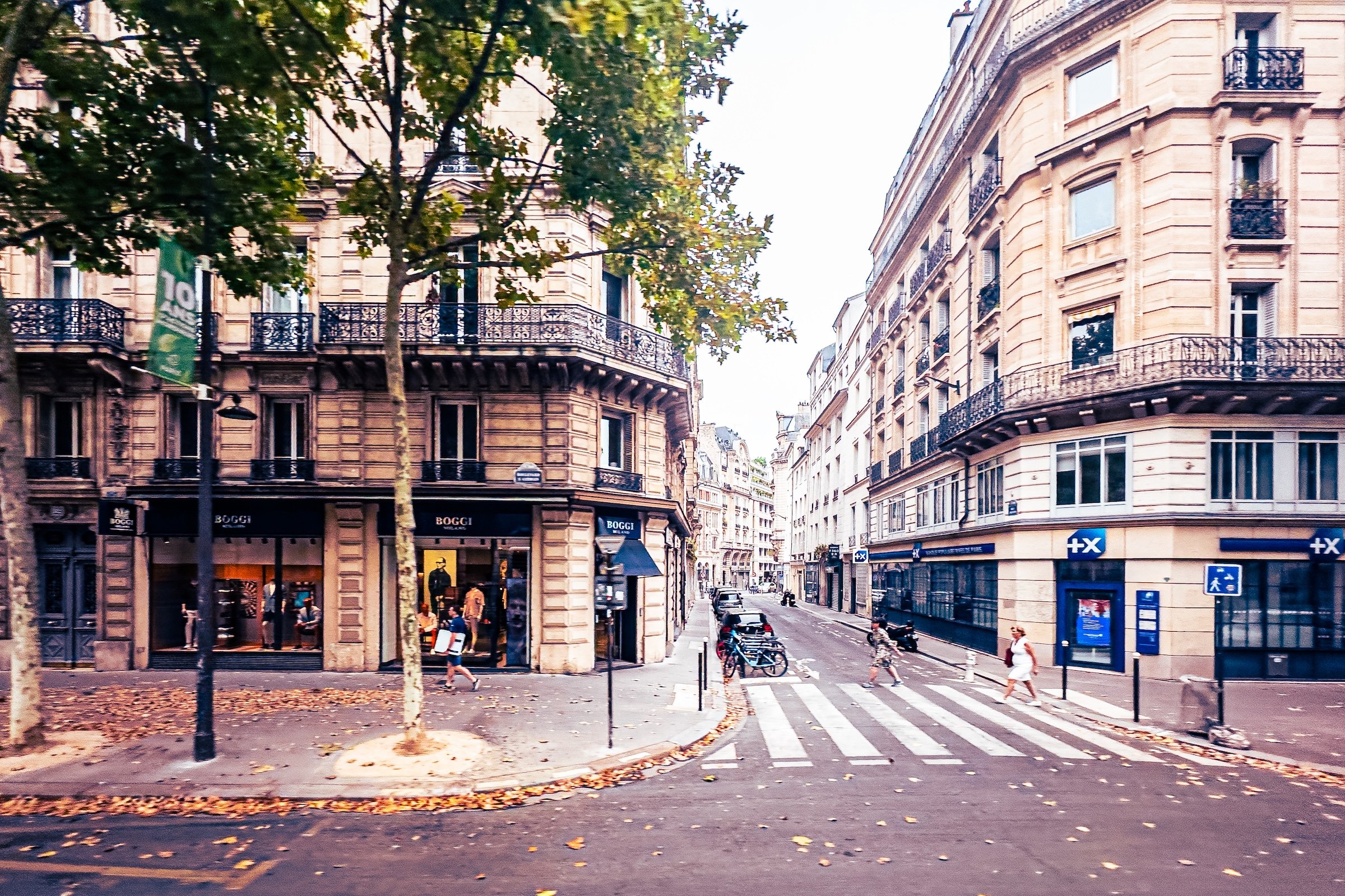 City street scene with historic beige buildings with wrought iron balconies, a traffic light, a tree, pedestrians, bicycles, and cars parked along the street.