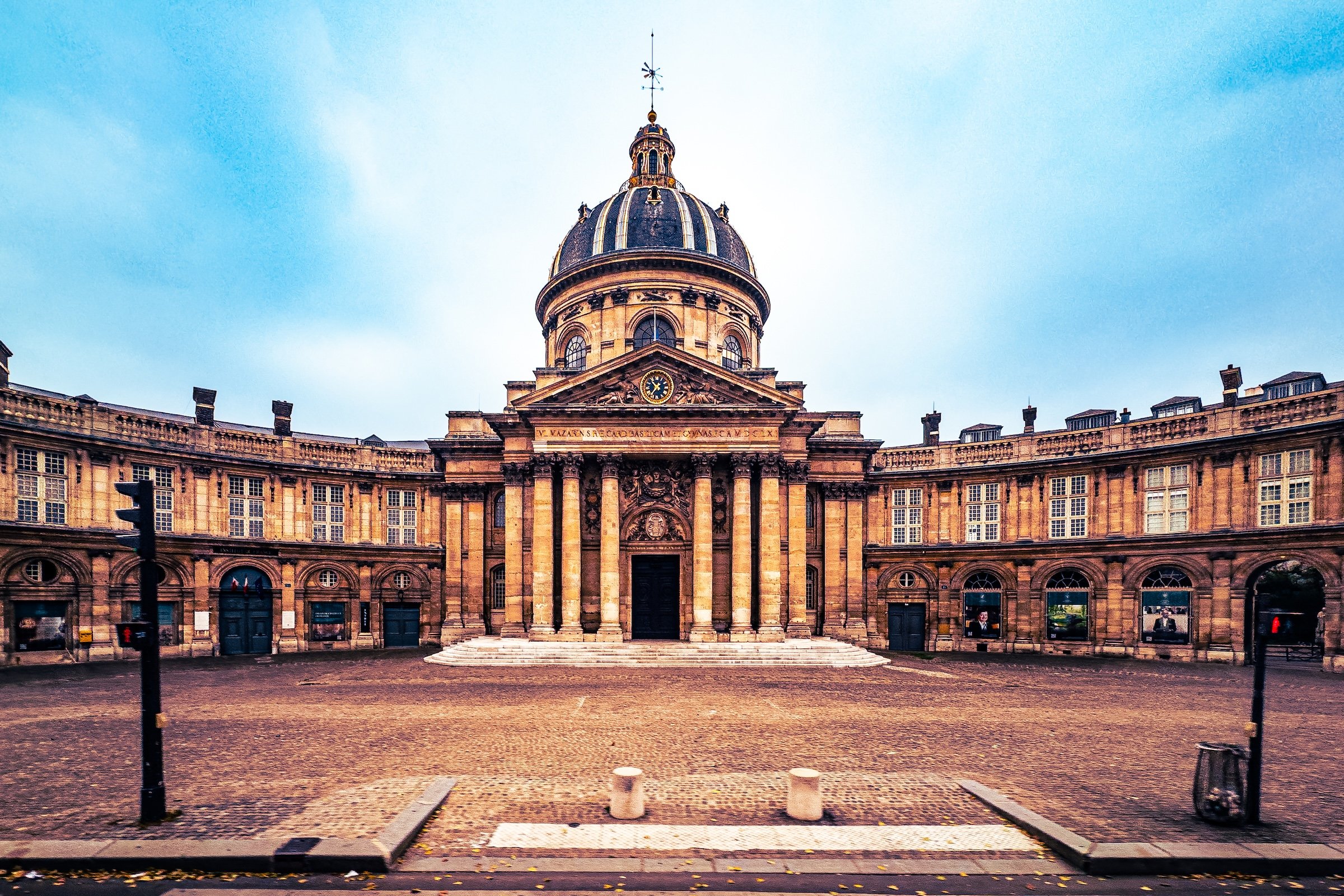 Front view of a historic building with a domed tower and clock, architecture with columns and detailed stonework, under a partly cloudy sky.