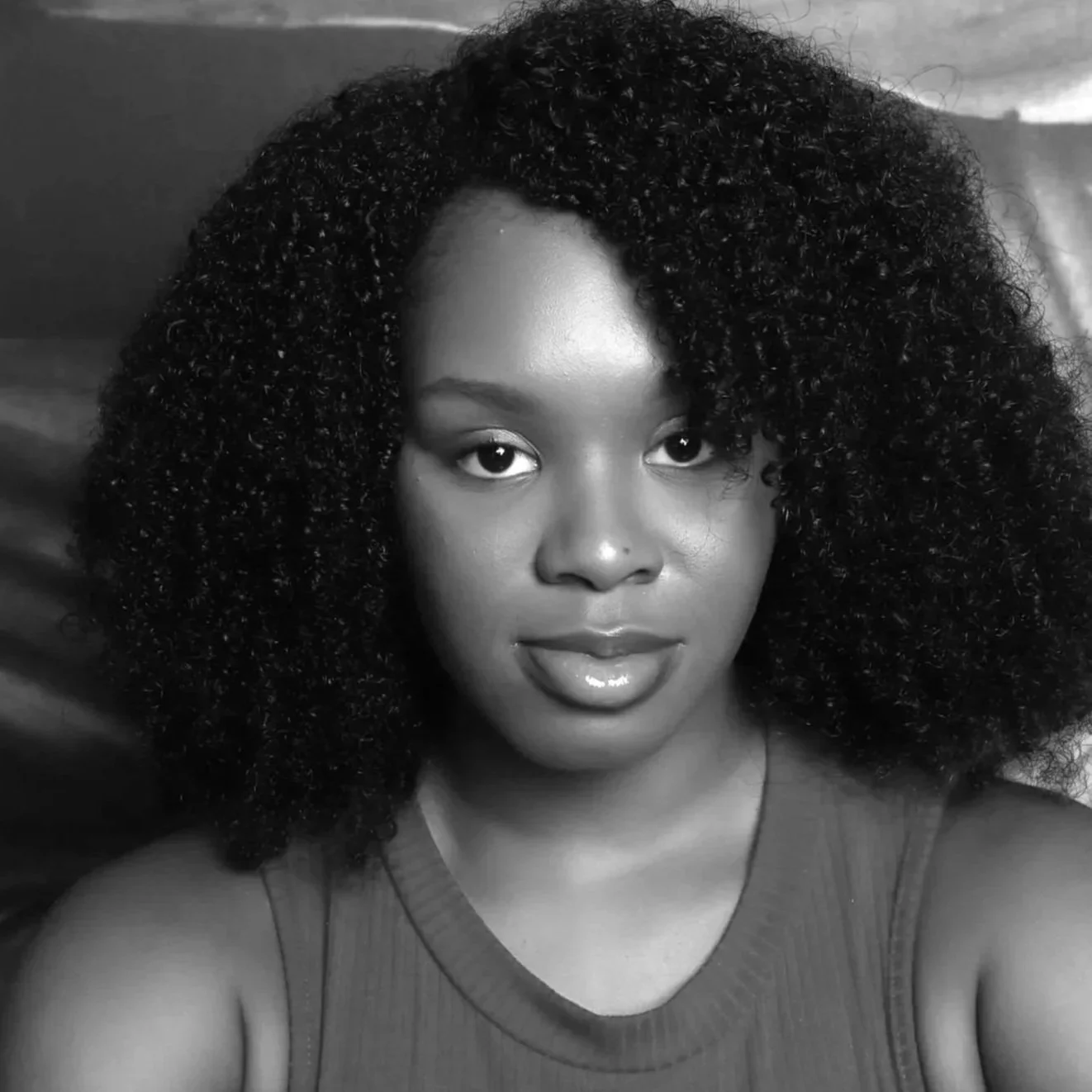 Black and white photo of a woman with voluminous curly hair, wearing a sleeveless top, looking directly at the camera.
