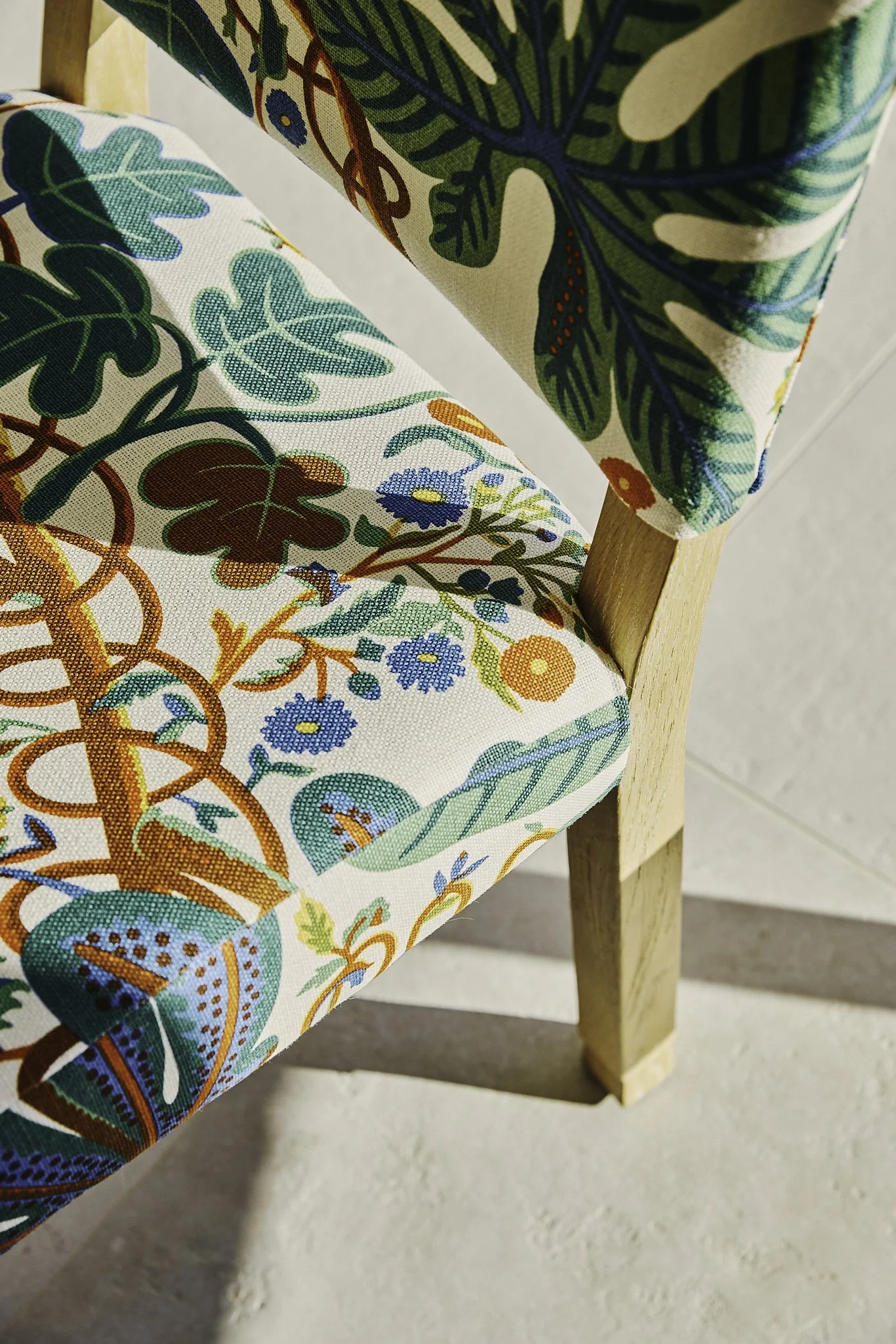 Close-up of a chair with a wooden leg and a seat and backrest upholstered in colorful fabric featuring a floral and leaf pattern
