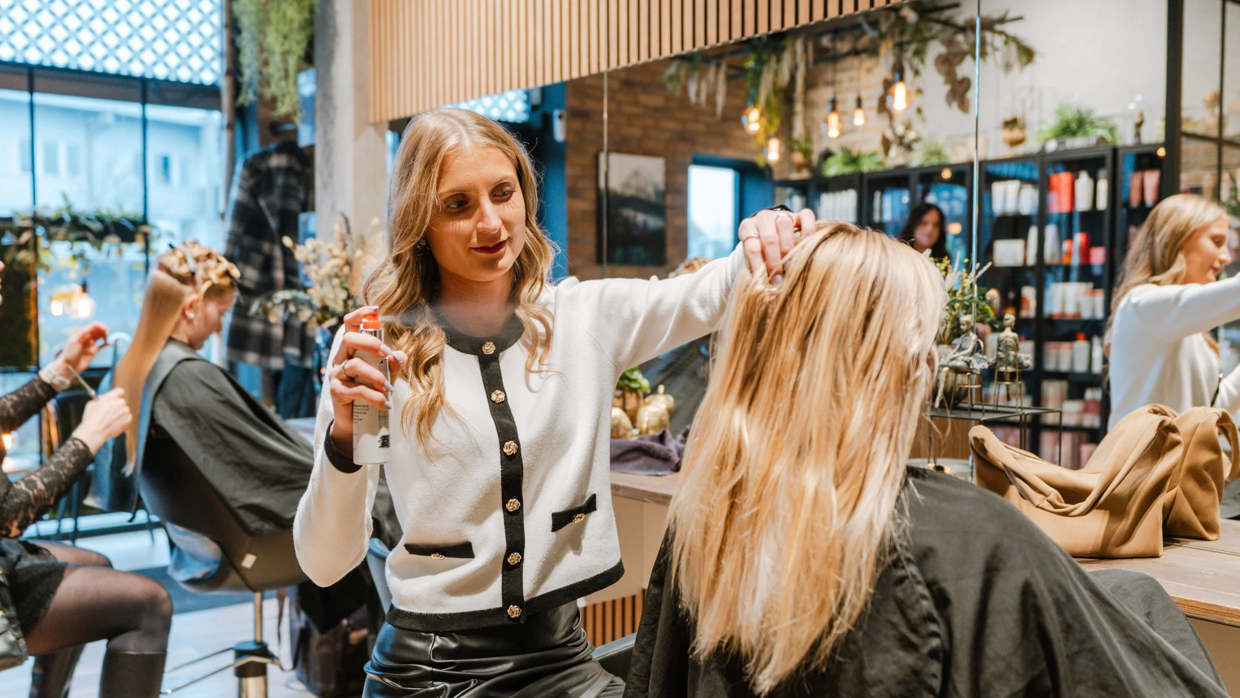 Kvinde får frisørbehandling i en frisørsalon med andre kunder