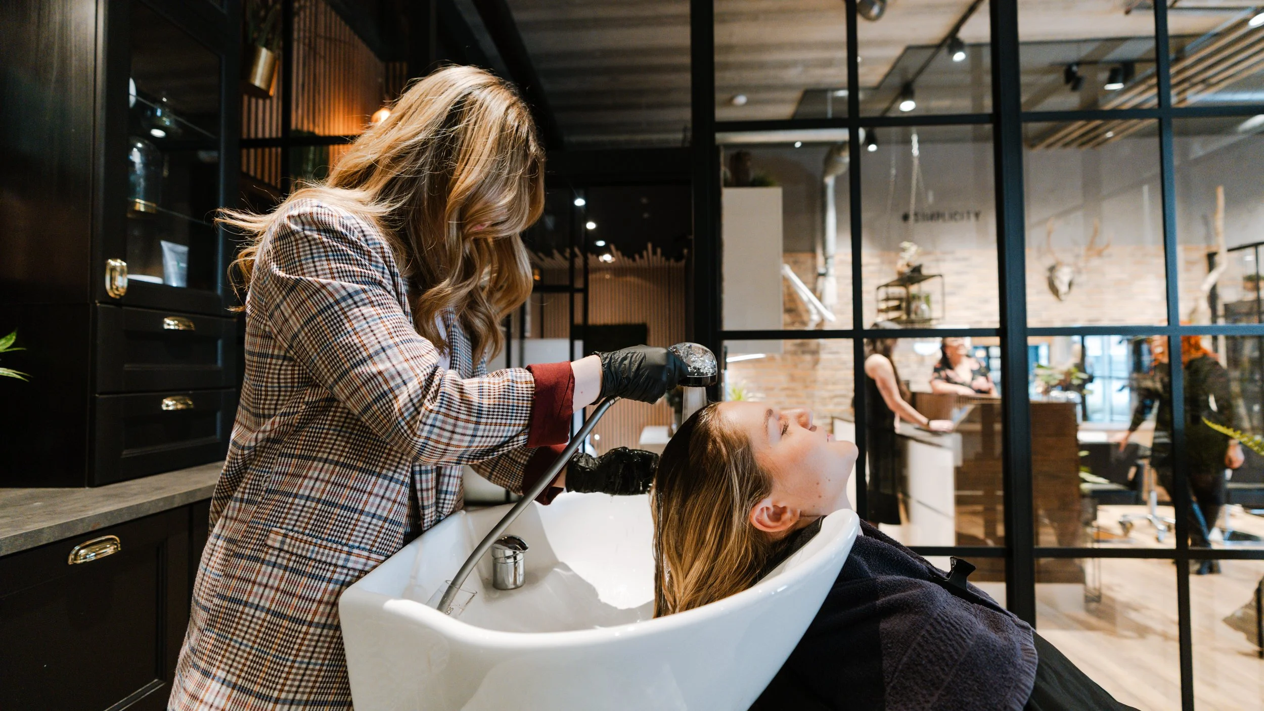Kvinde får vasket sit hår i en frisørsalon, mens en frisør bruger en vaskehoved.