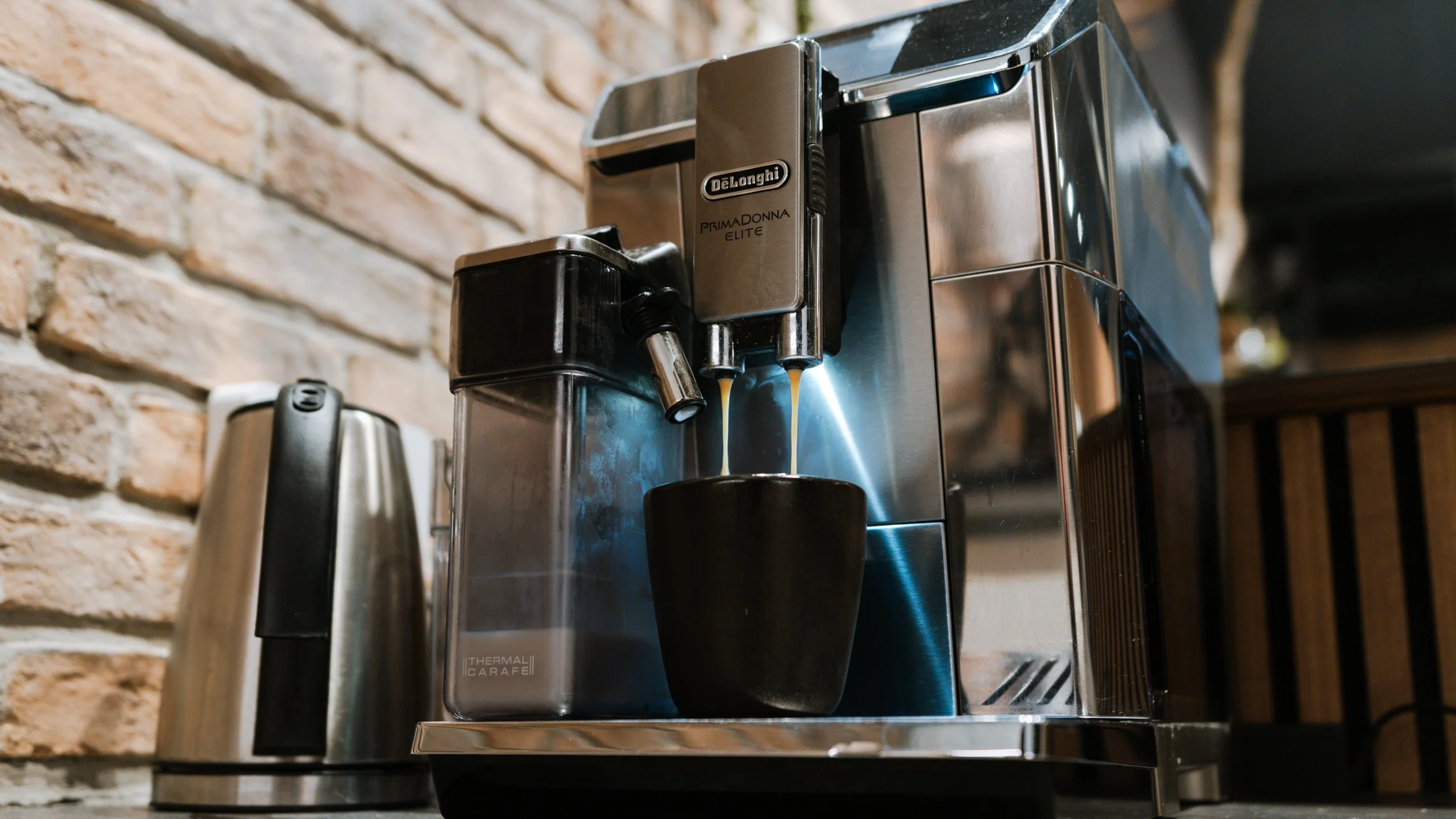 Kaffemaskine, der laver espresso, med en sort kop under udløbet, i en frisørsalon med brændt murstensvæg.