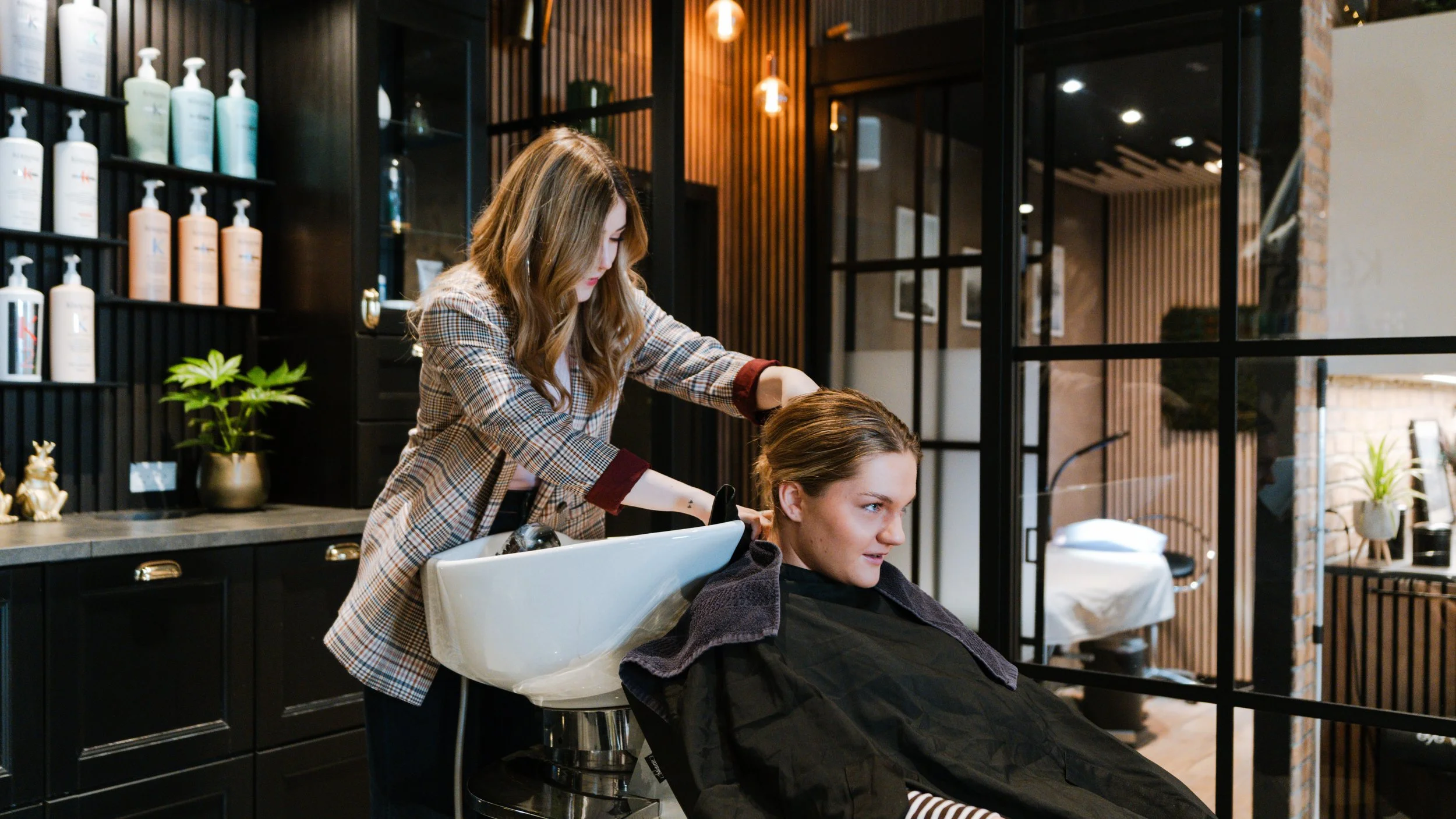 Kvindelig frisør vasker en kundes hår i en moderne frisørsalon.