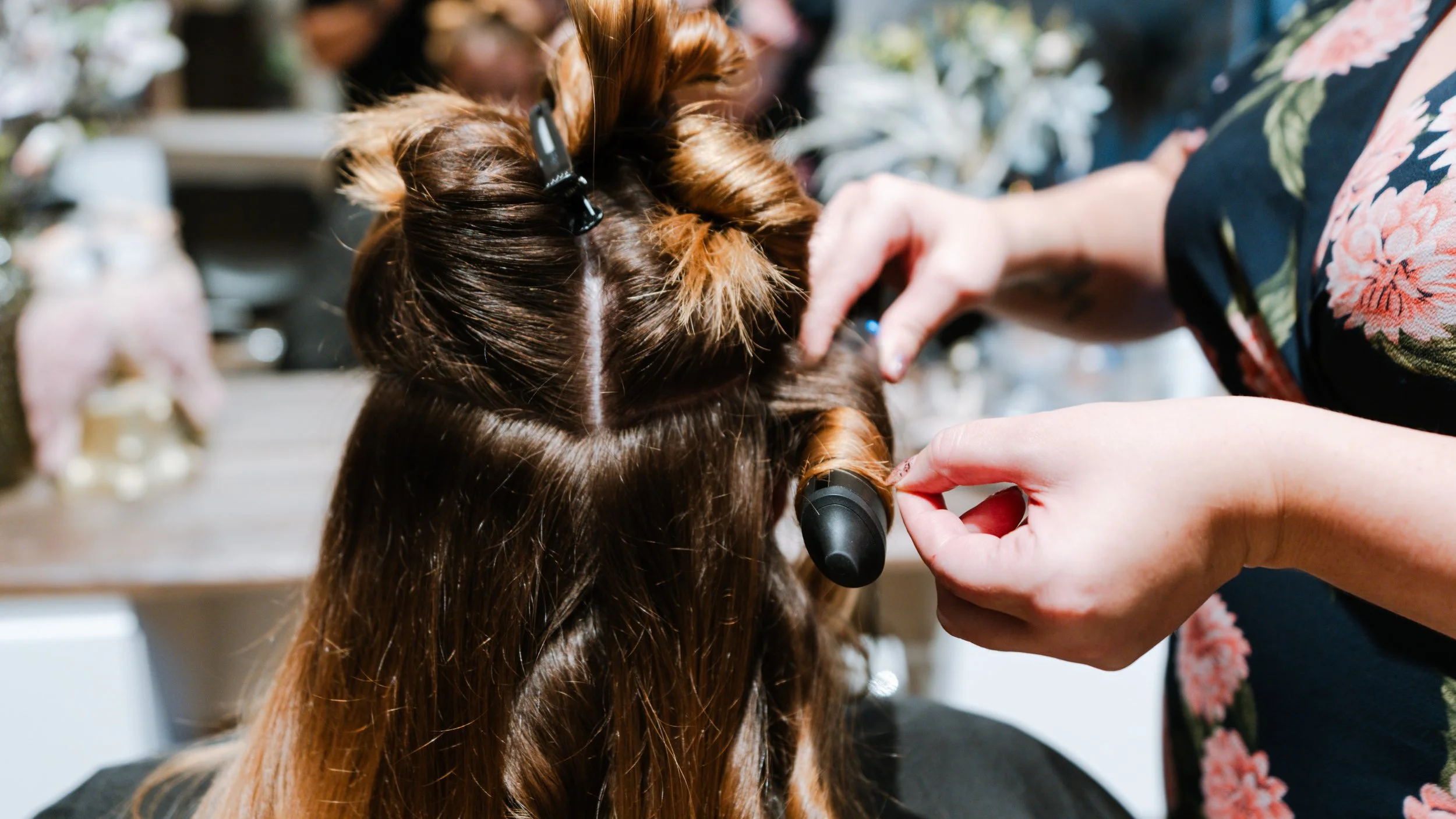 En frisør, der styler en kvindes lange, brune hår ved at bruge ruller.