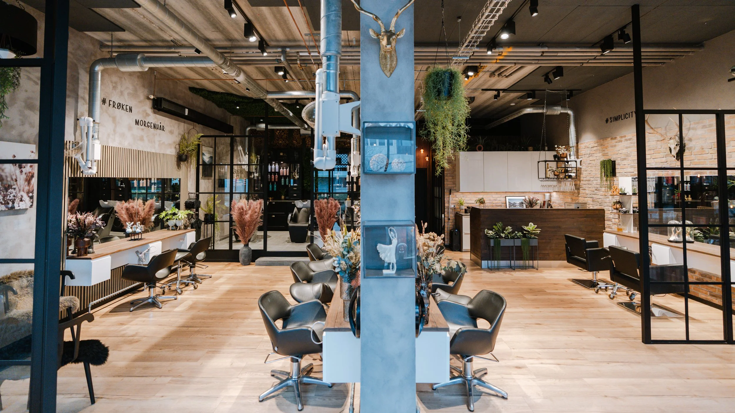 Indretning af en moderne frisørsalon med spejle, frisørstole og dekorative planter.