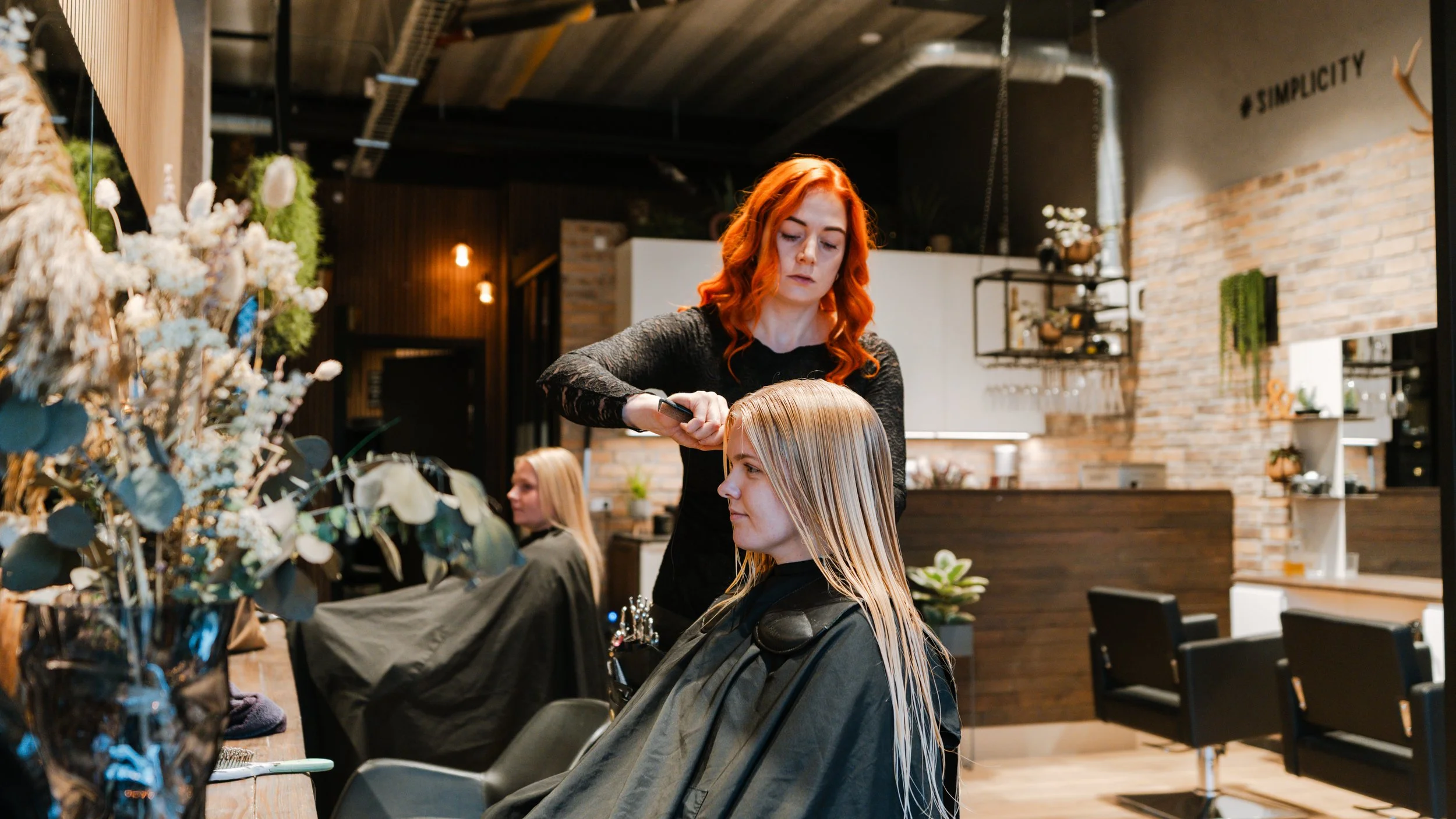 En frisør, der klipper en blond kvindes hår i en moderne salon med træaccenter og brændte vægge.