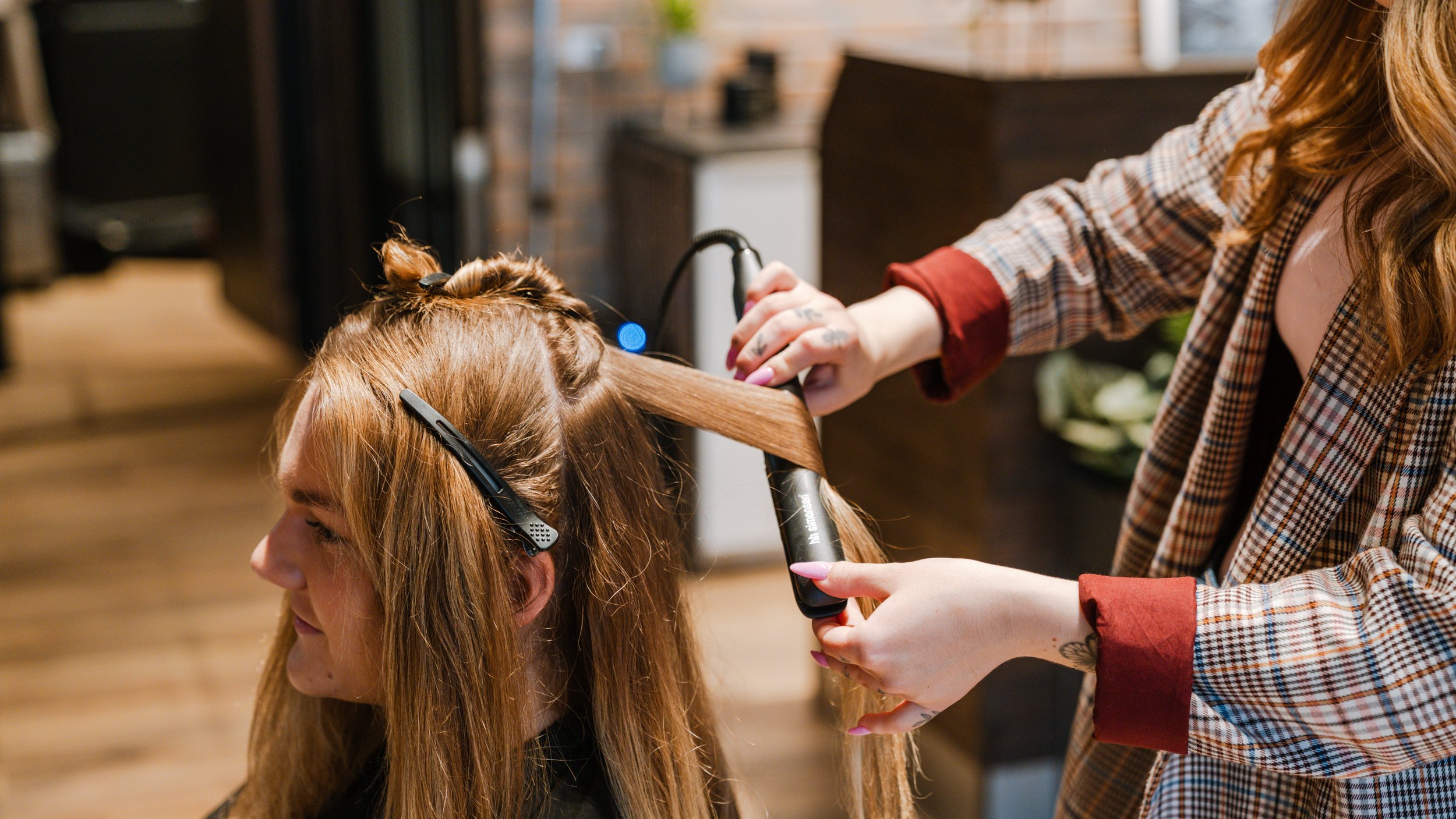 En frisør, der styler en kvindes hår med en glattejern.