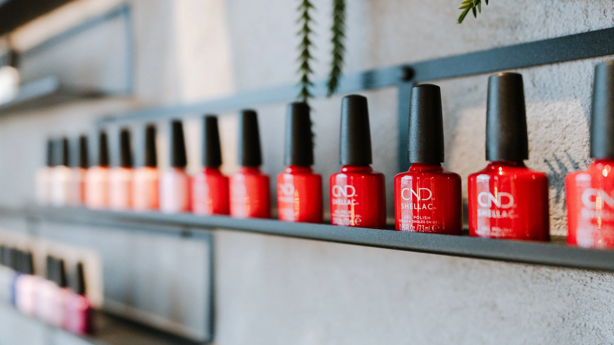 Rækker af røde neglelakflasker på en hylde mod en betonvæg.