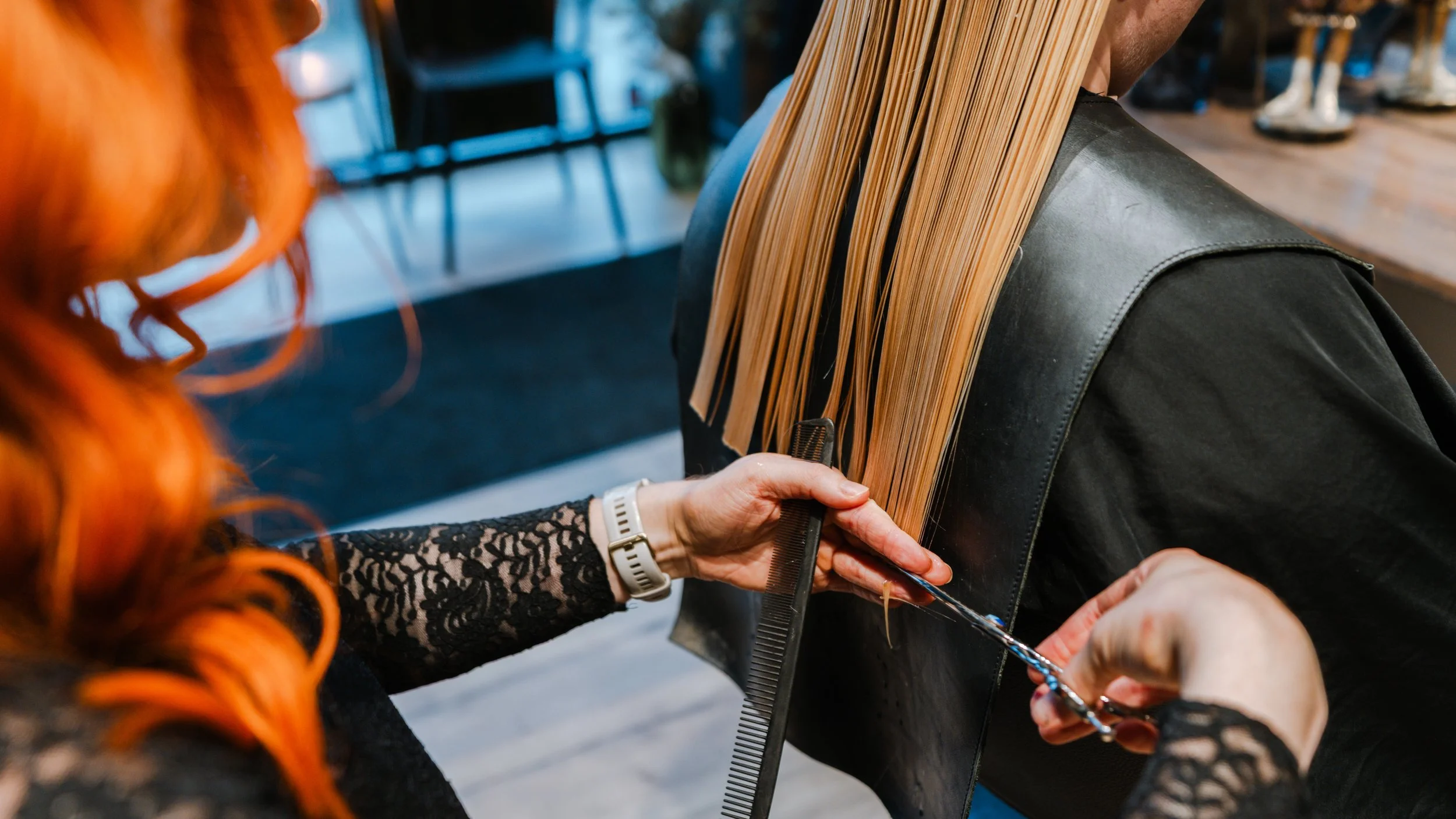 En frisør med rødt hår klipper en persons lange blonde hår i en frisørsalon.