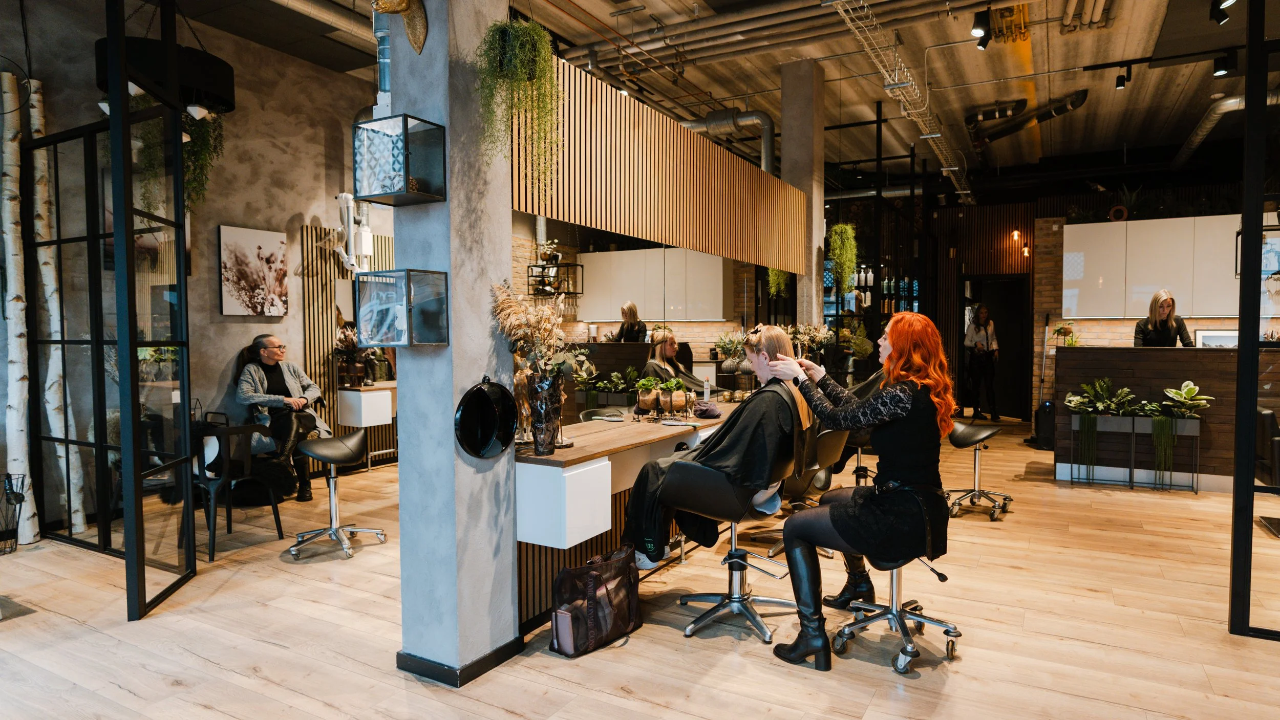 Personer der får en frisørbehandling i en moderne frisørsalon med træ- og murstensdetaljer, planter og belysning.