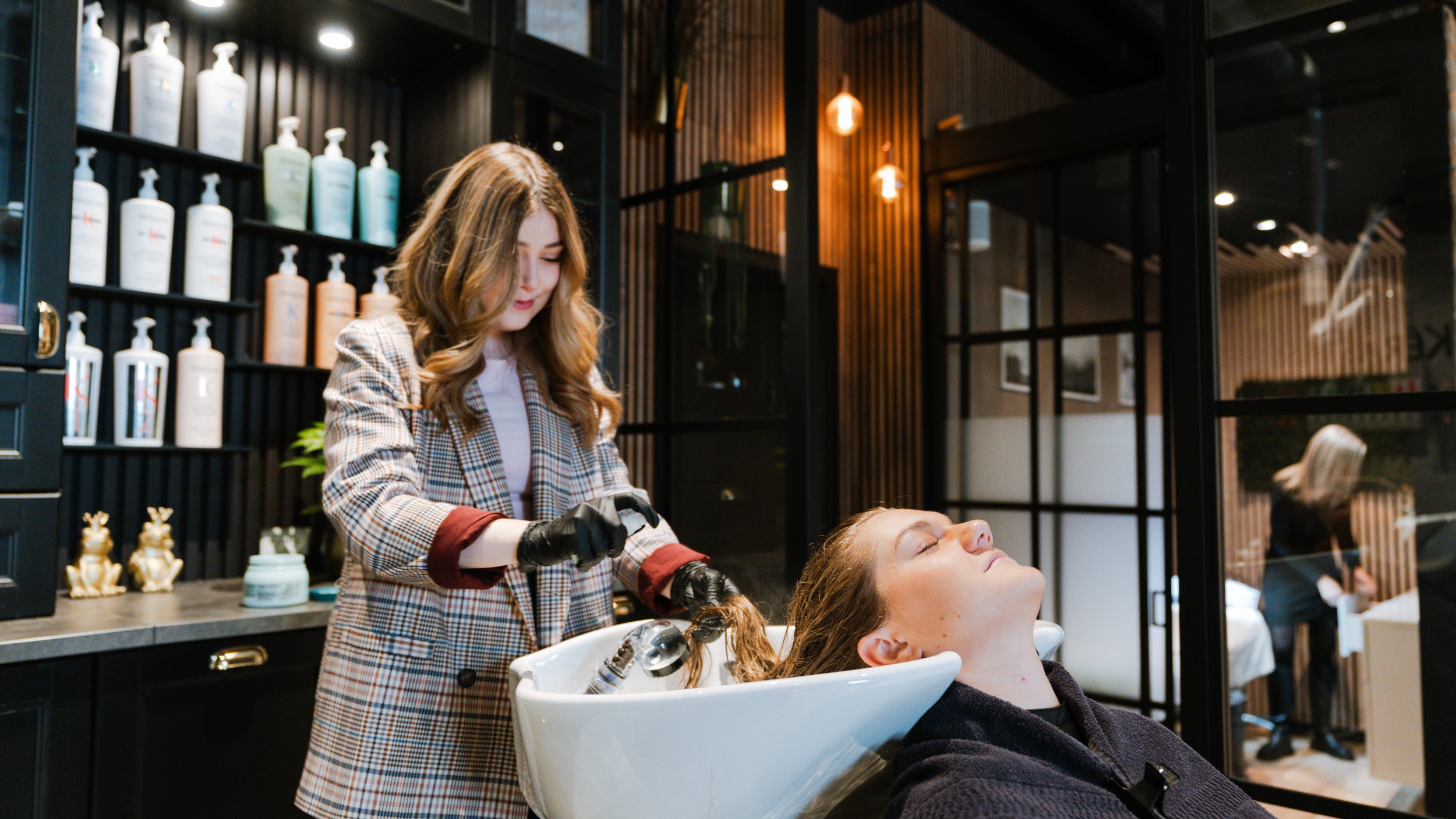 En kvinde får vasket og blondet sit hår i en frisørsalon, mens en frisør bruger en vaskebænk og professionelt udstyr.