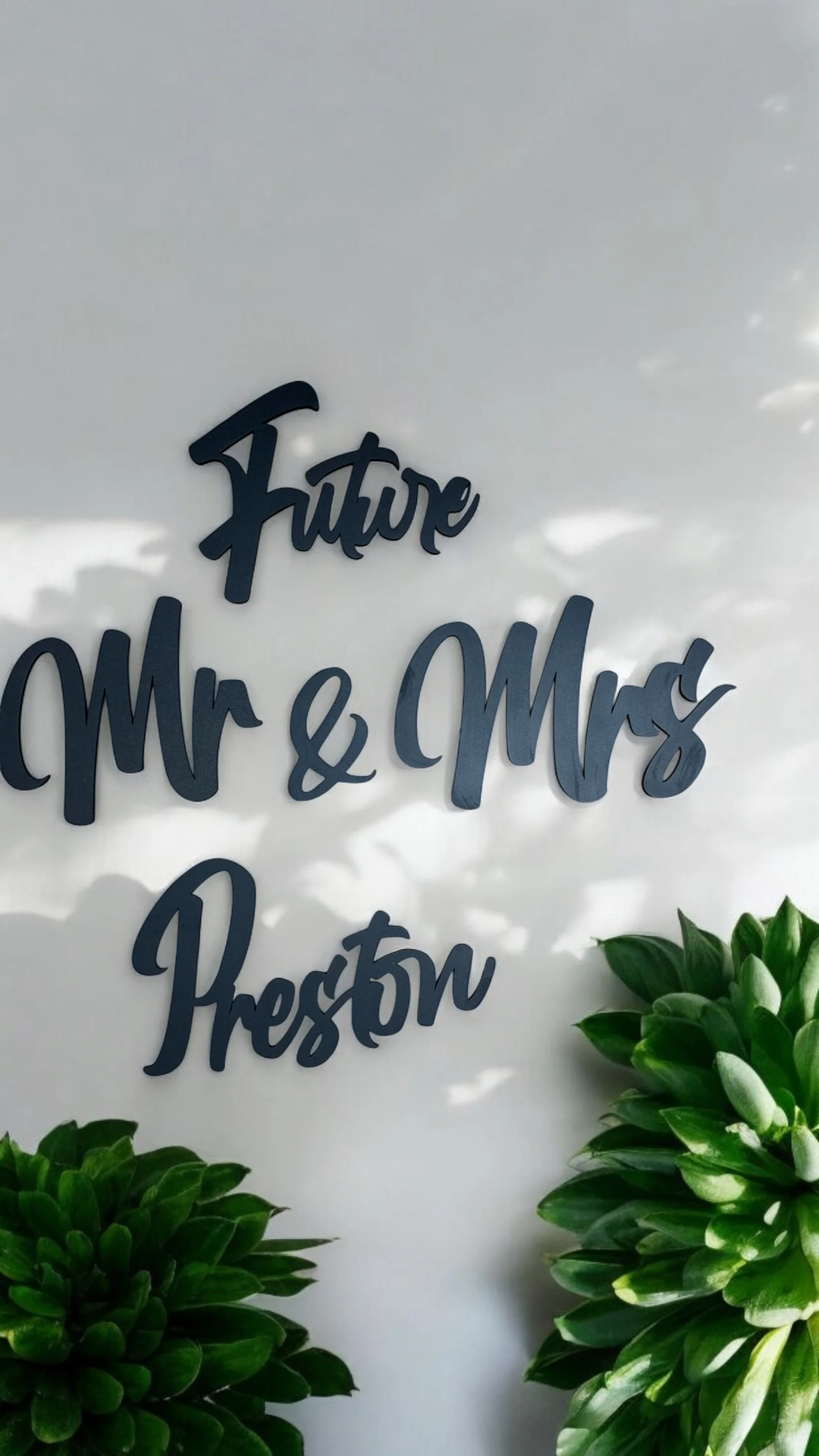 Decorative wall with words 'future' and 'Mr. & Mrs.' and a bunch of green plants in the foreground.