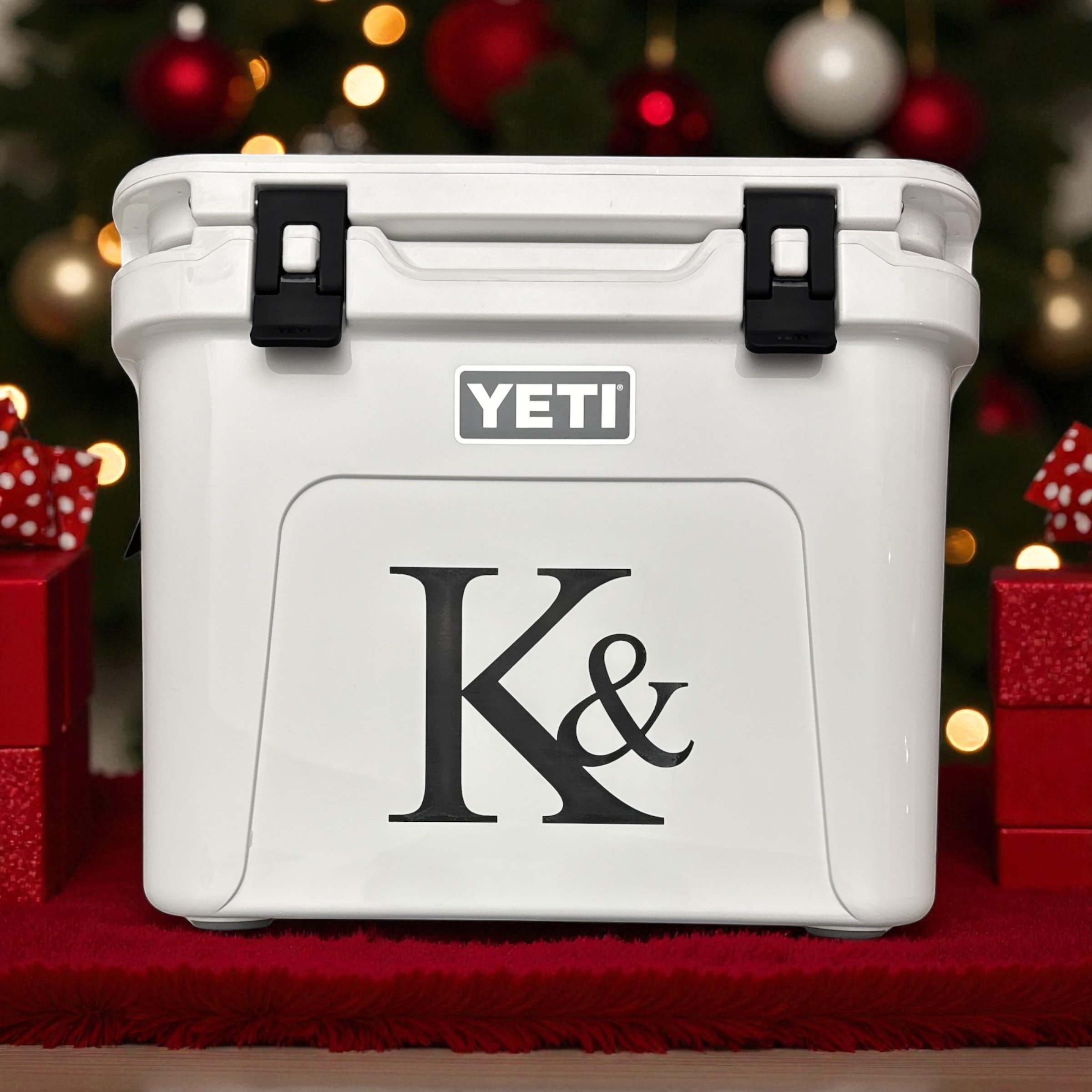 Close-up of a white YETI cooler with black latches, set against a festive background with Christmas lights, ornaments, and red decorations.