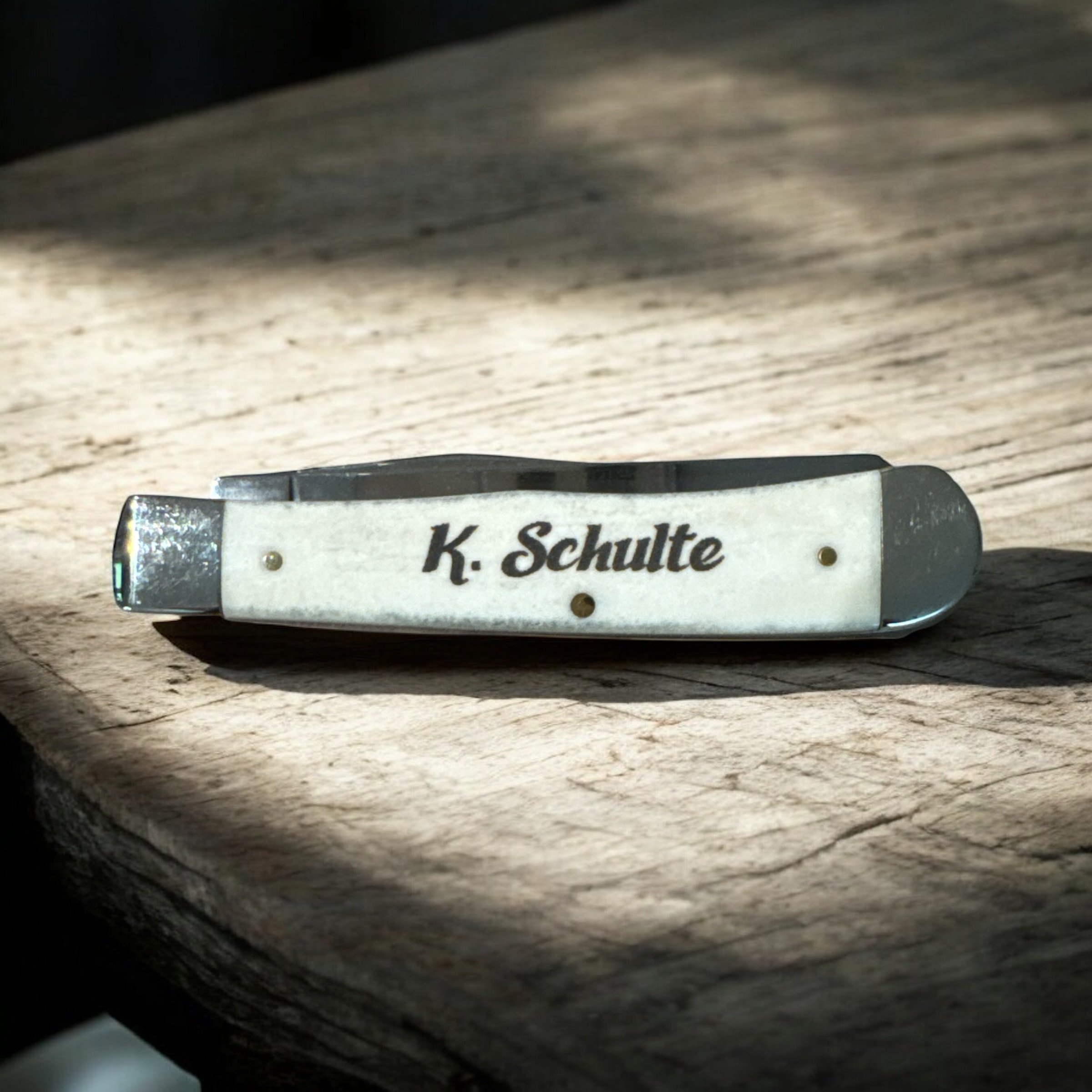 Close-up of a knife with engraved text on its blade, resting on a wooden surface.