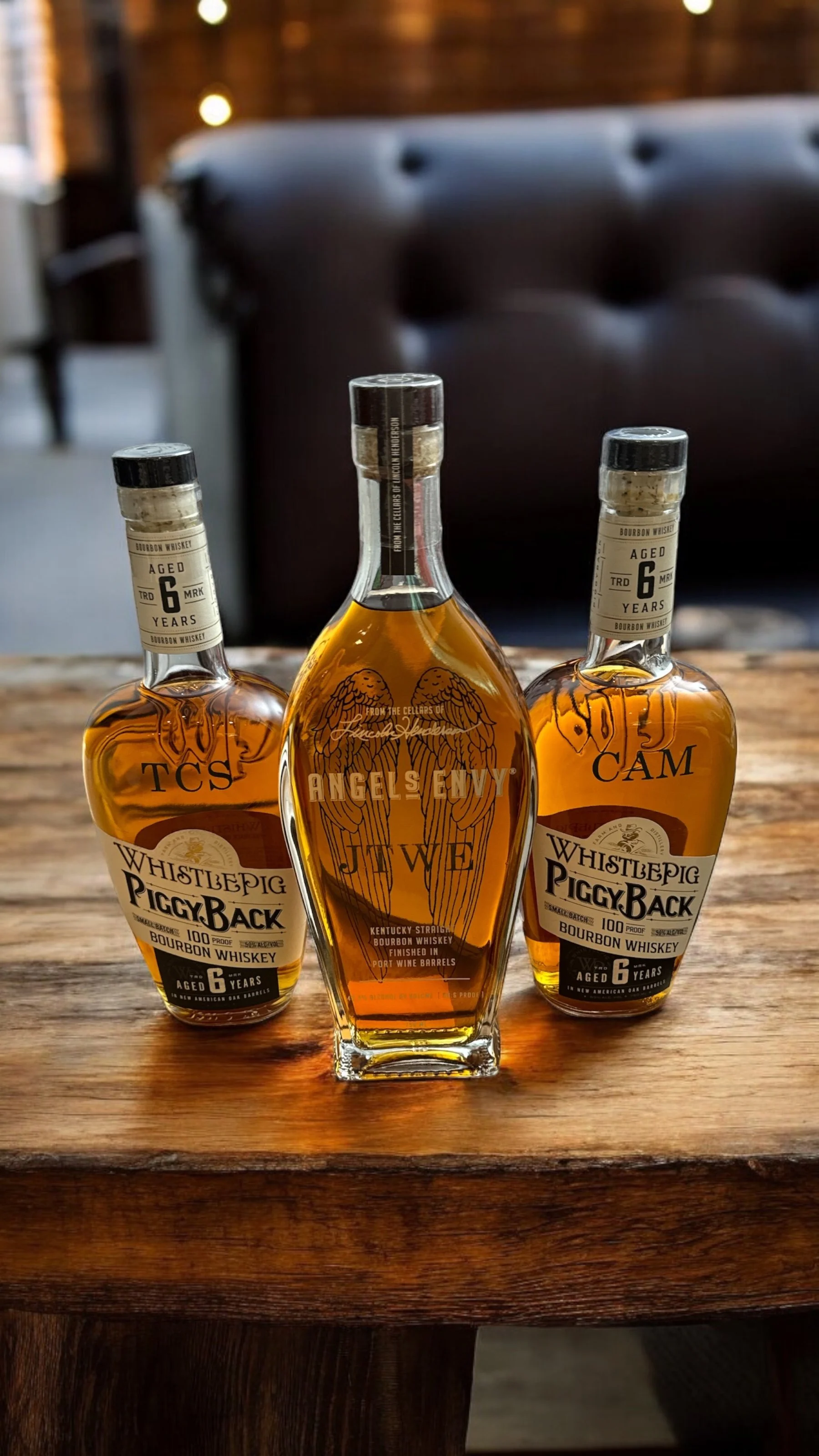 Three bottles of whiskey on a wooden table, with a dark blurry background.