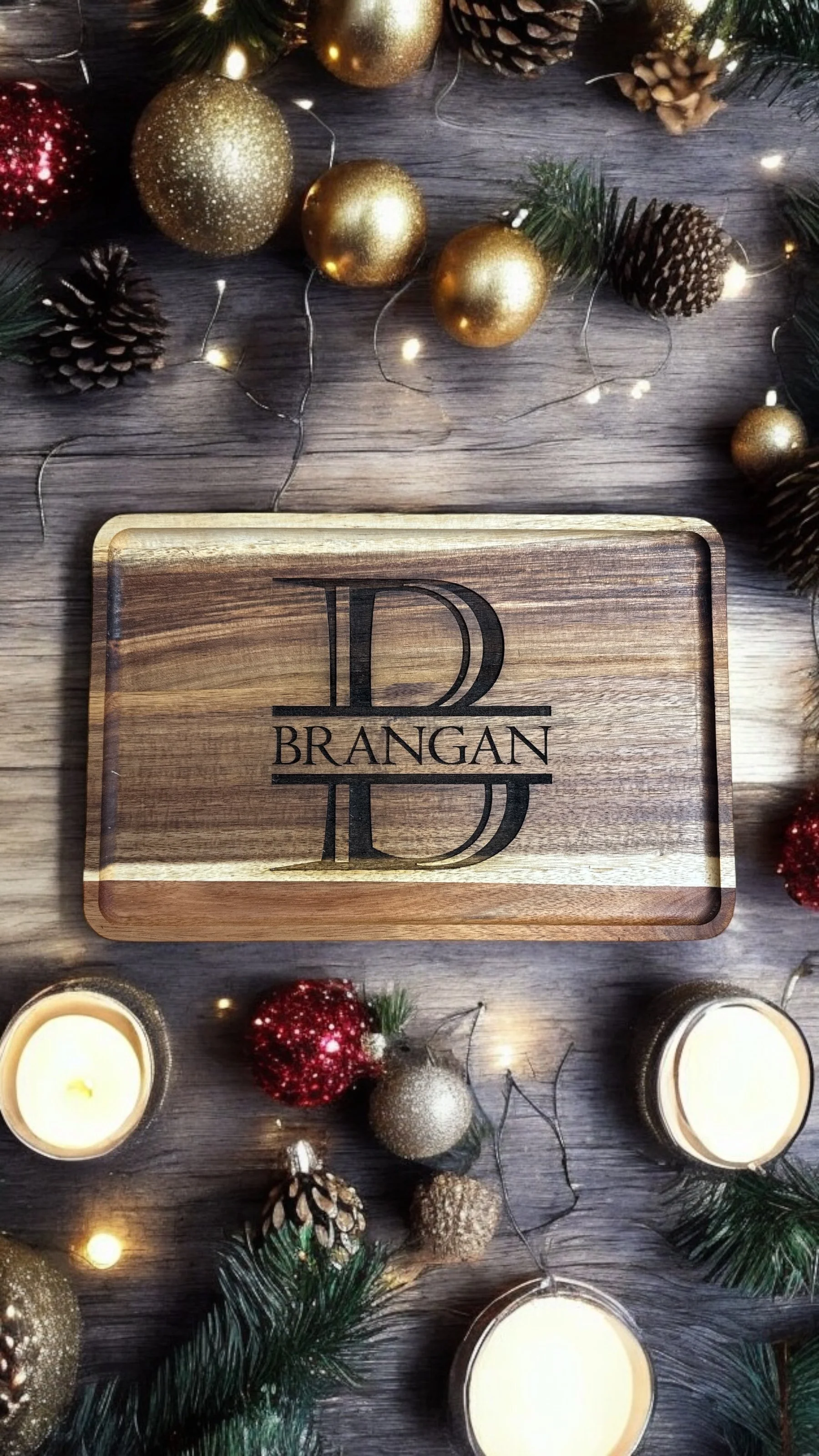 A wooden box with the text 'Brangan' and a stylized letter 'B' on it, surrounded by holiday decorations including gold, red, and silver ornaments, pinecones, candles, and part of a Christmas tree with lights and greenery.