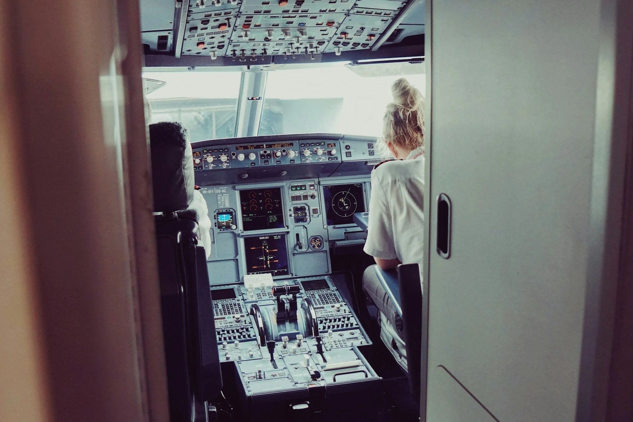 View of an airplane cockpit with two crew members, one with a bun hairstyle, seated at the controls.