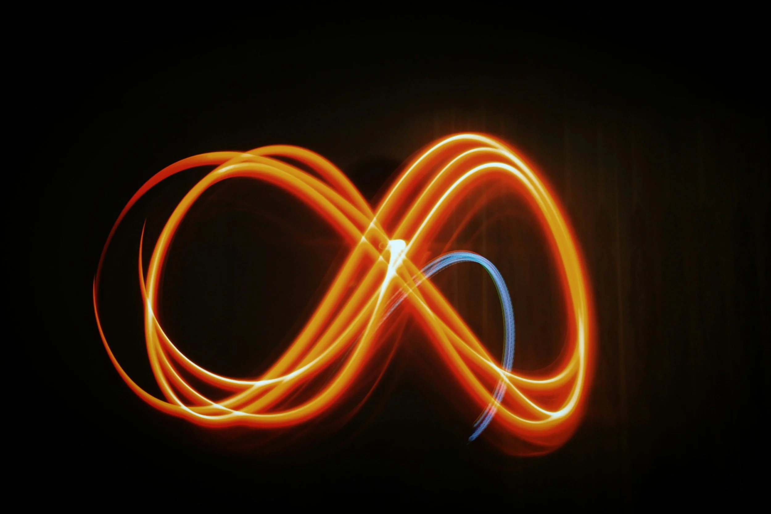 Light trails in the shape of an infinity symbol with bright orange and blue colors on a black background.