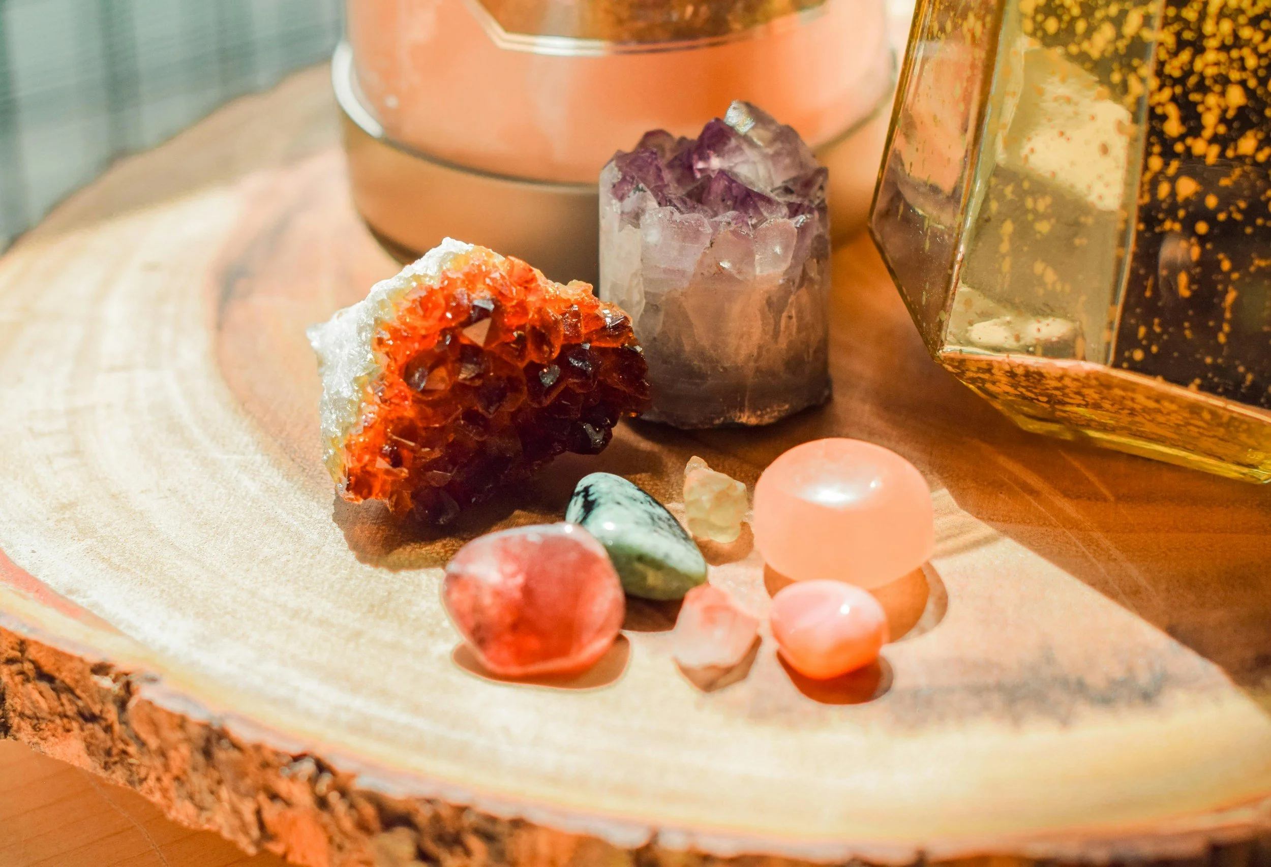 Collection of colorful crystals and gemstones on a wooden surface, with a book and decorative objects in the background.