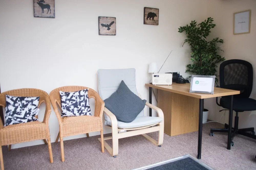 Office waiting area with wicker chairs, a wooden desk with a computer, a plant, a framed certificate, and wall decorations featuring animal silhouettes.