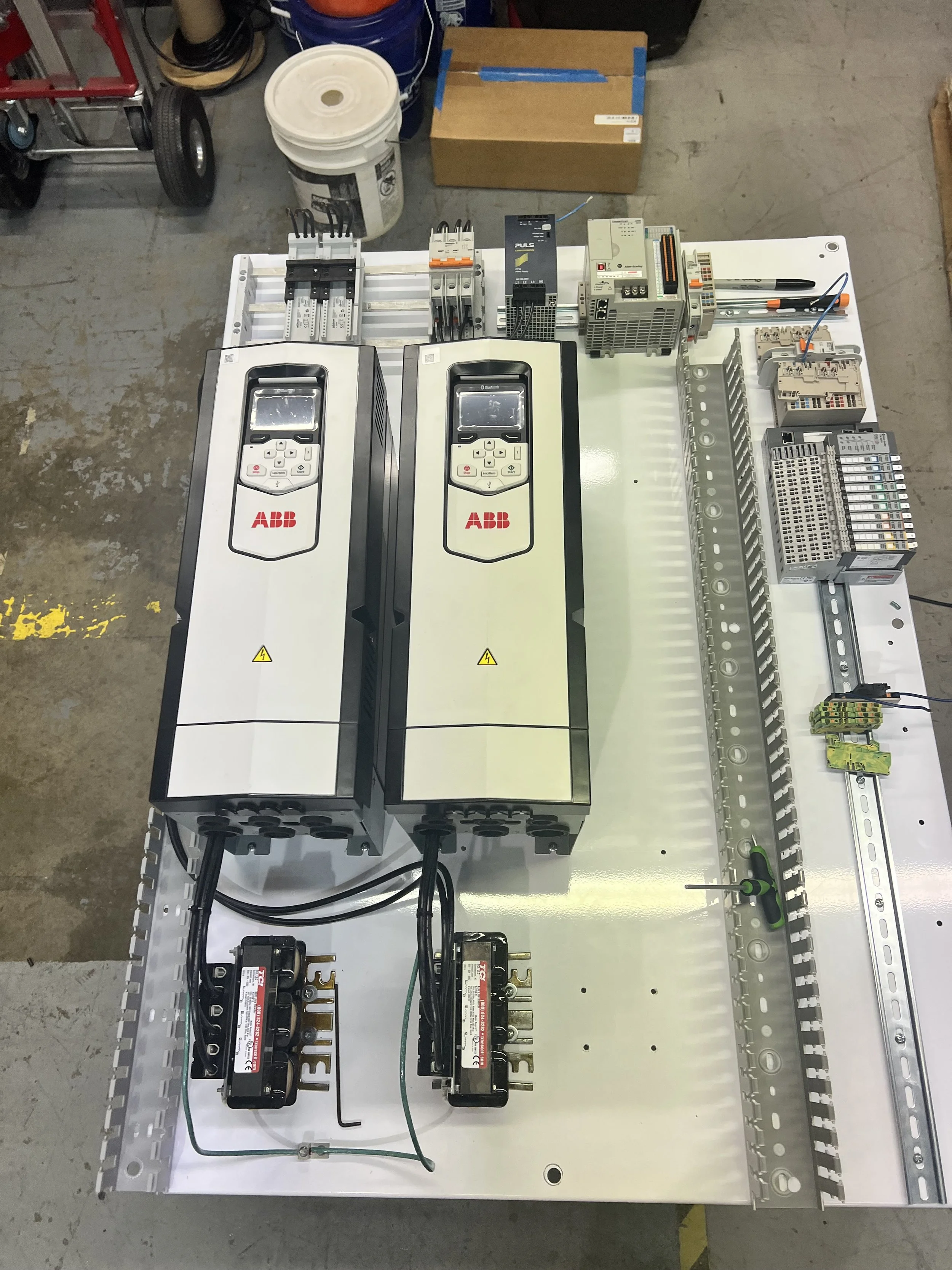 Industrial electrical control panel with ABB variable frequency drives, relays, and terminal blocks mounted on a metallic enclosure.