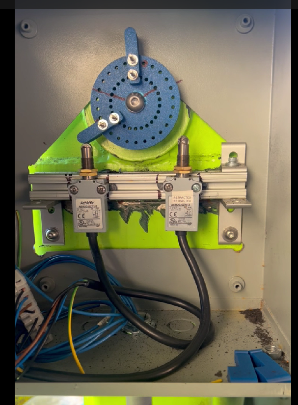 Electrical components inside a metal enclosure, including a blue rotating dial, two black relays, and various wires connected to the components.