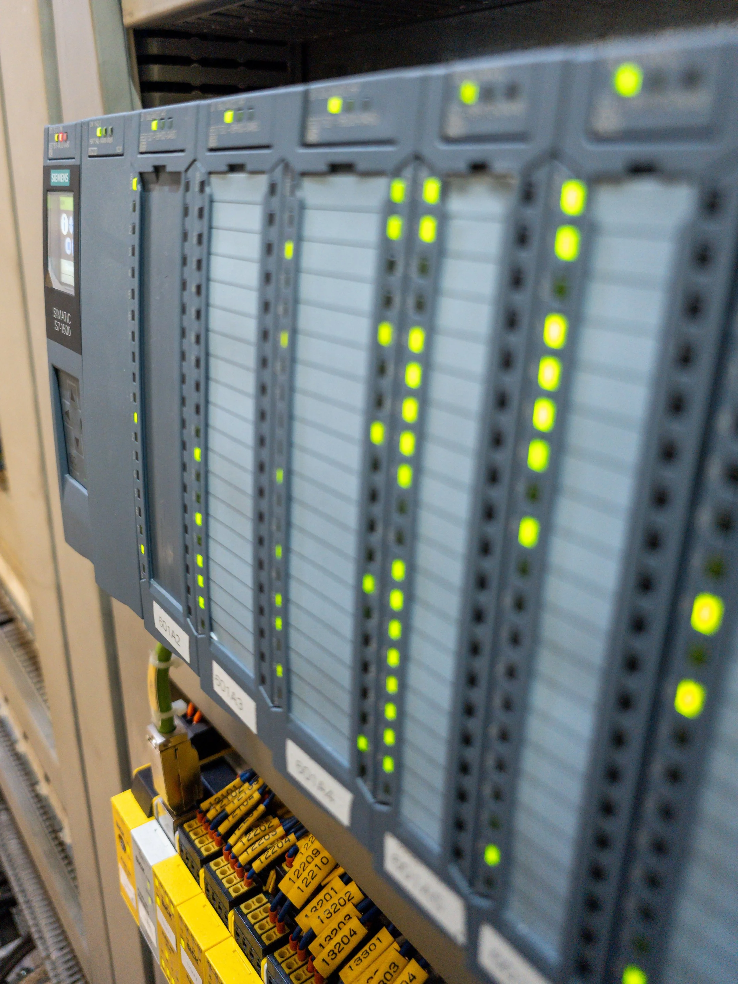 Industrial programmable logic controllers (PLCs) mounted on a panel with indicator lights and wired modules, used in automation and control systems.