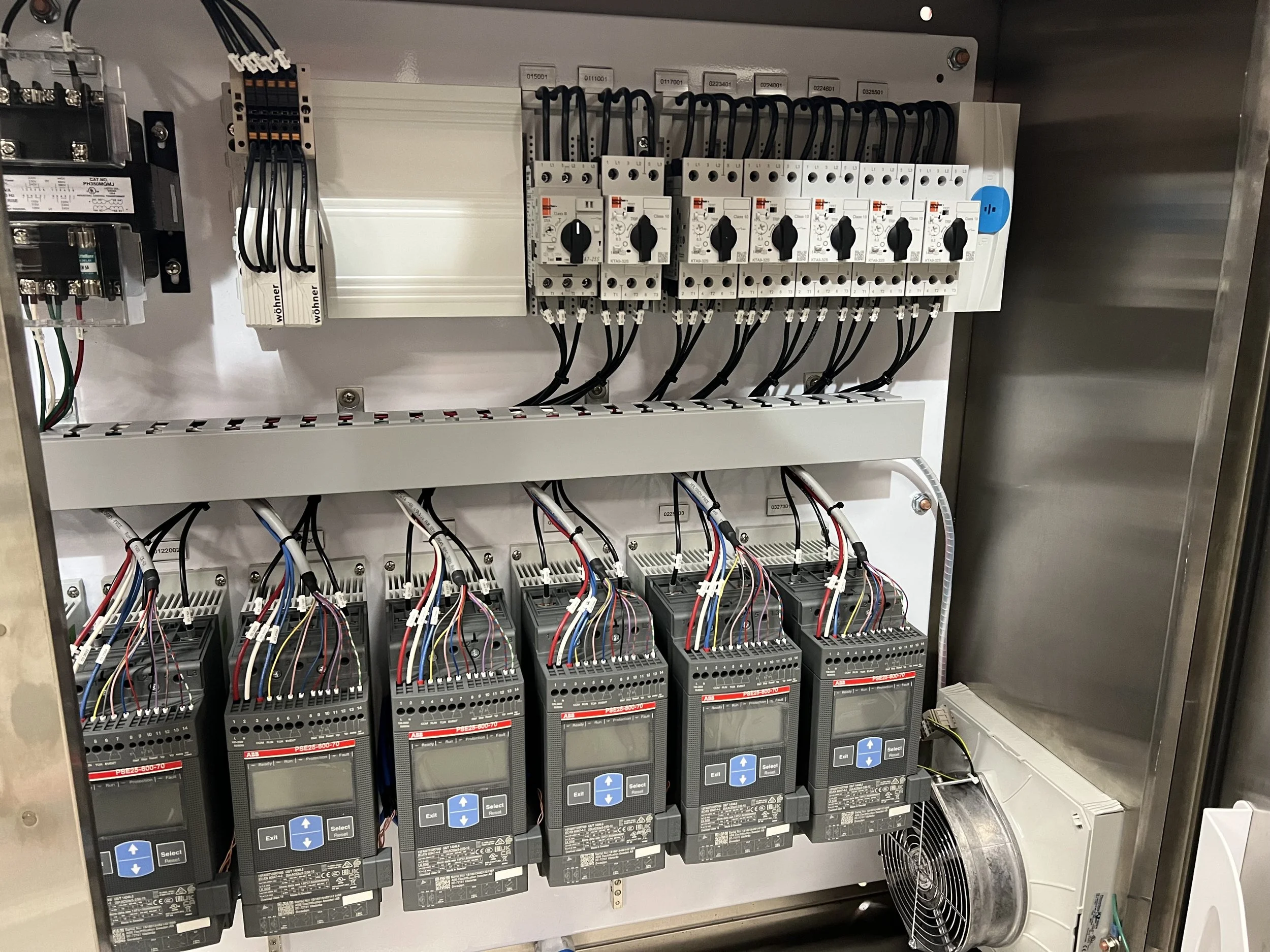 An electrical control panel featuring circuit breakers, relays, and variable frequency drives with multiple wires connected, mounted inside a metal enclosure.