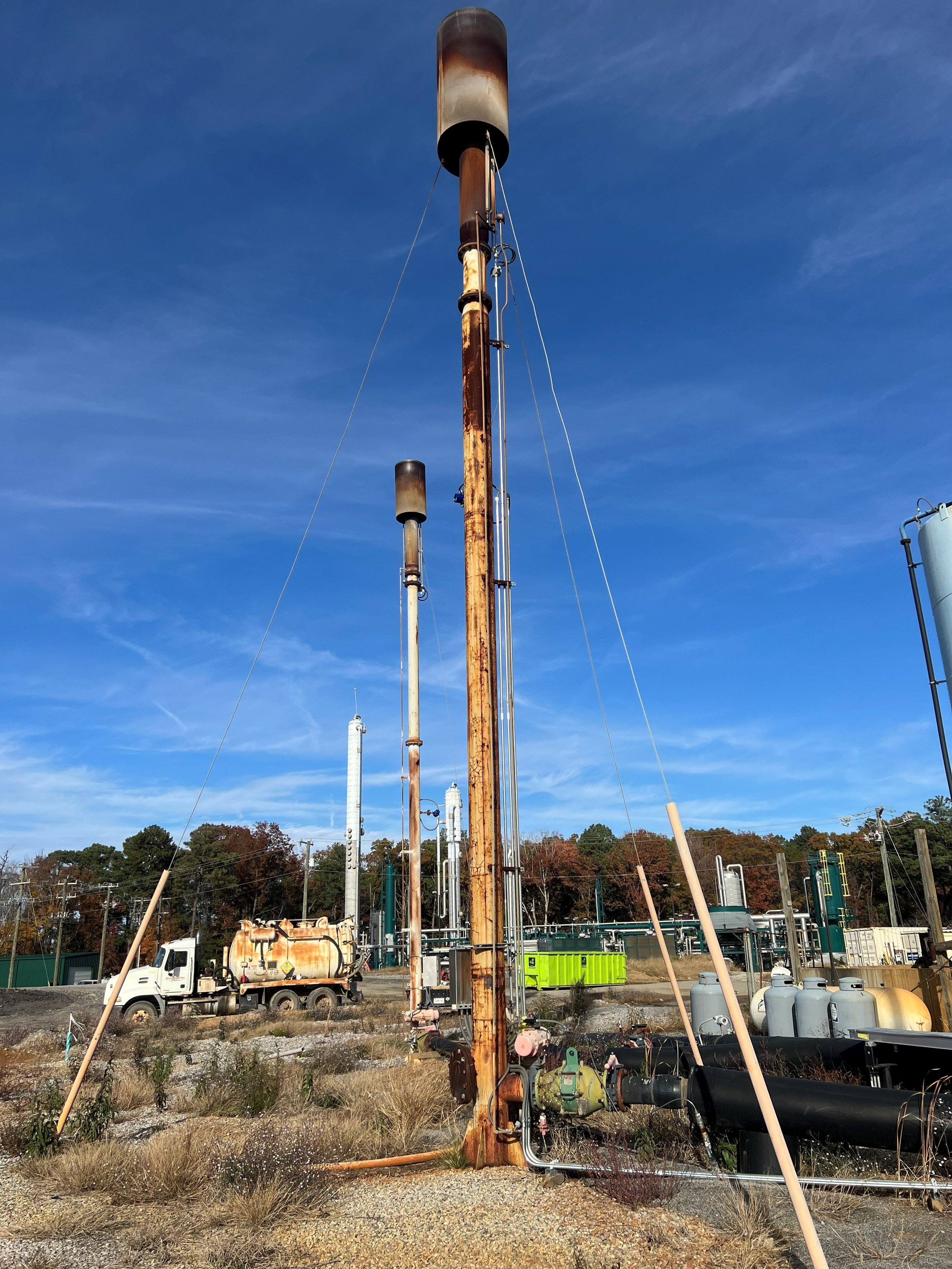 Industrial storage tanks with rusted pipes and equipment at an industrial site under a clear blue sky.