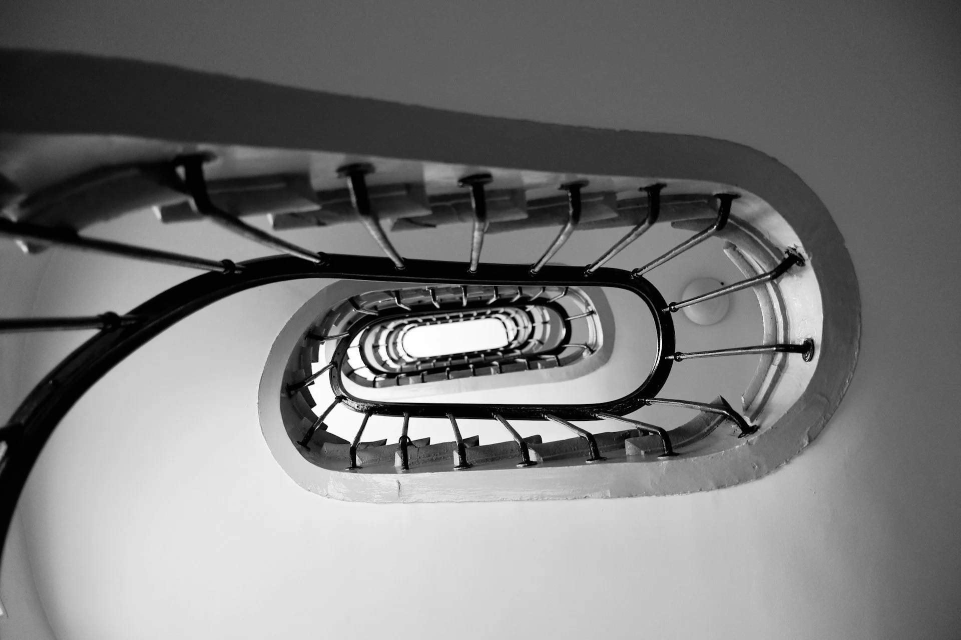 Black and white photo of a spiral staircase viewed from below, focusing on the elegant, swirling design