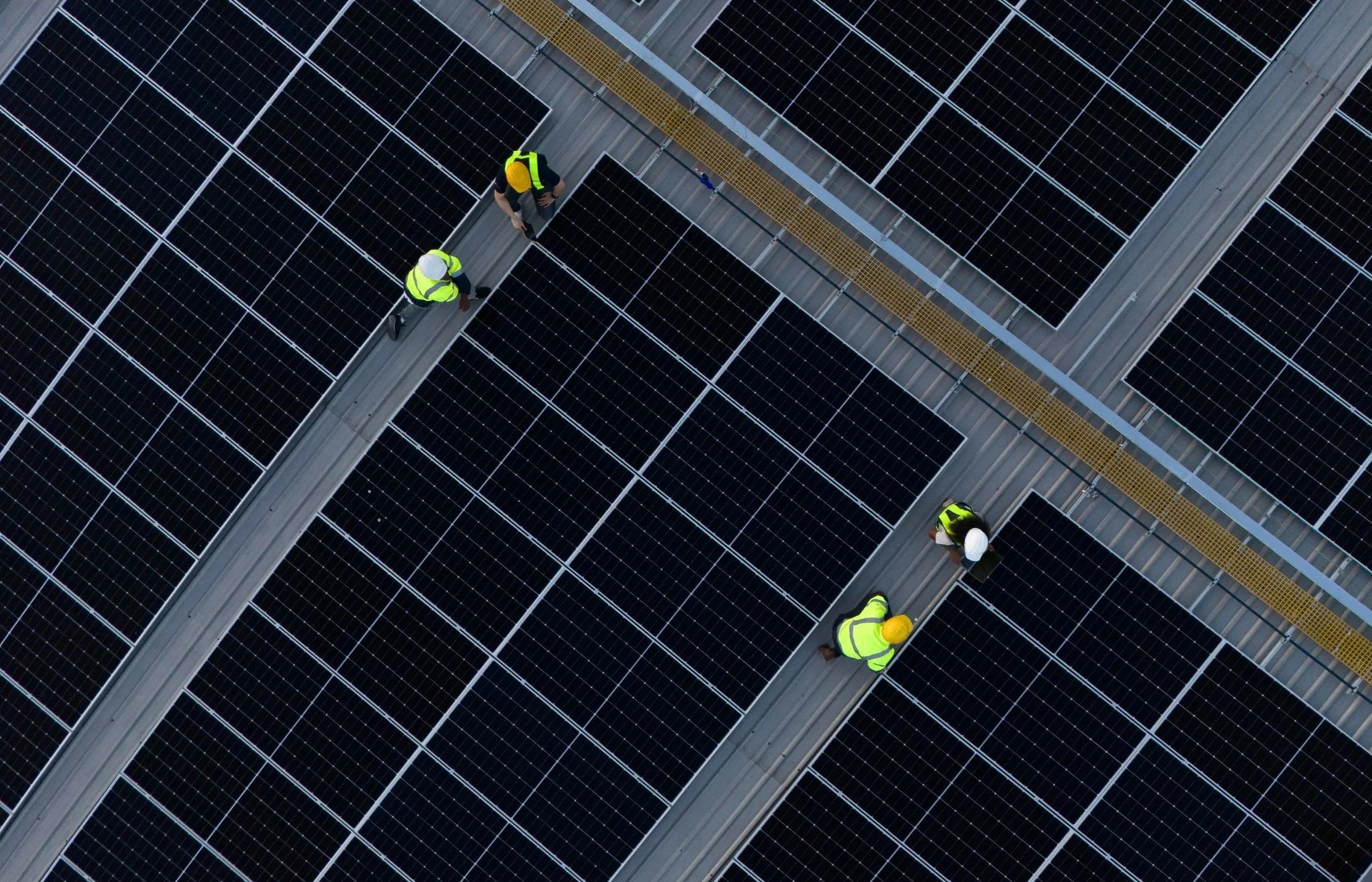 Travailleurs en sécurité avec des casques et des gilets réfléchissants inspectant des panneaux solaires sur un toit.