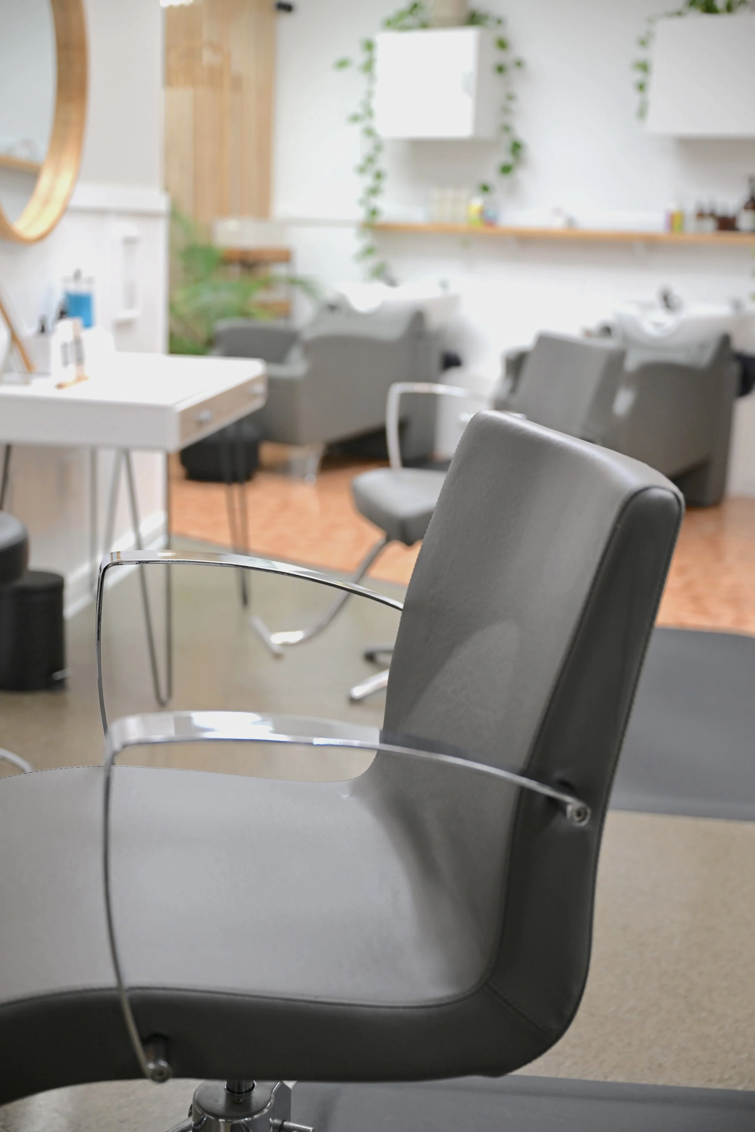 Empty salon chairs in a hair salon with a row of washbasins on the wall in the background. Clean, calm atmosphere