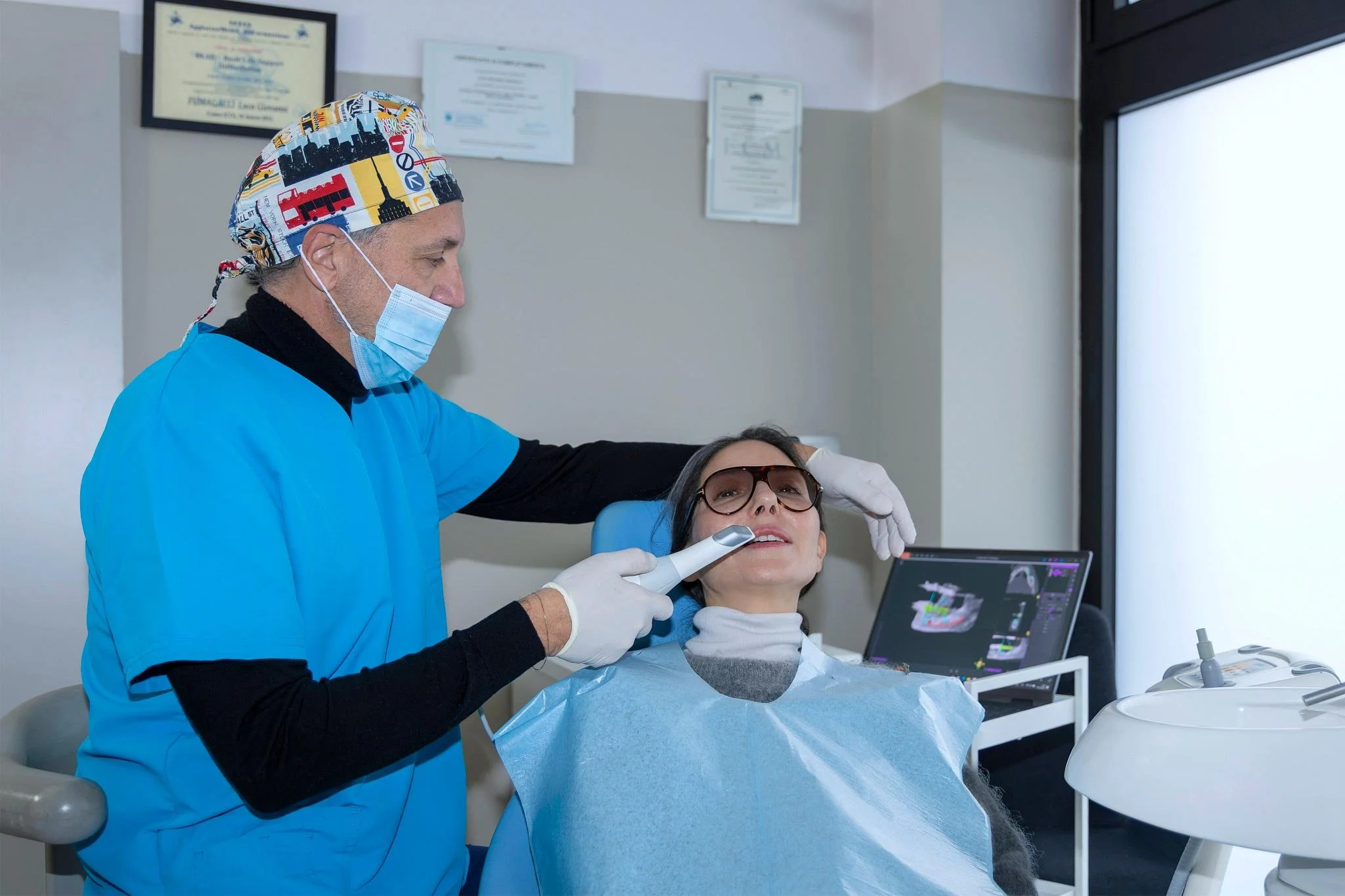 Dentista che esamina una paziente seduta in una clinica odontoiatrica, con apparecchiature mediche e certificati alle pareti