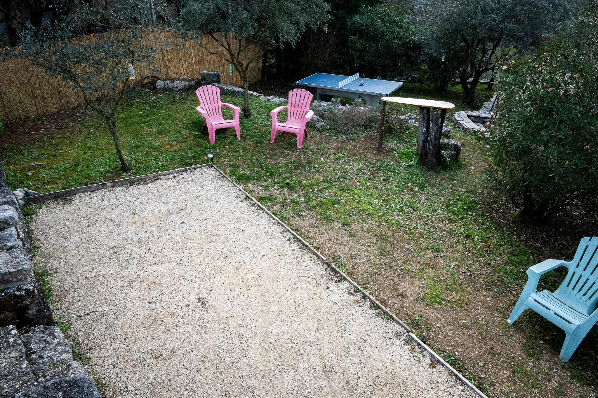 Un terrain de pétanque, une table de ping-pong, un terrain de sable, et une chaise bleue.