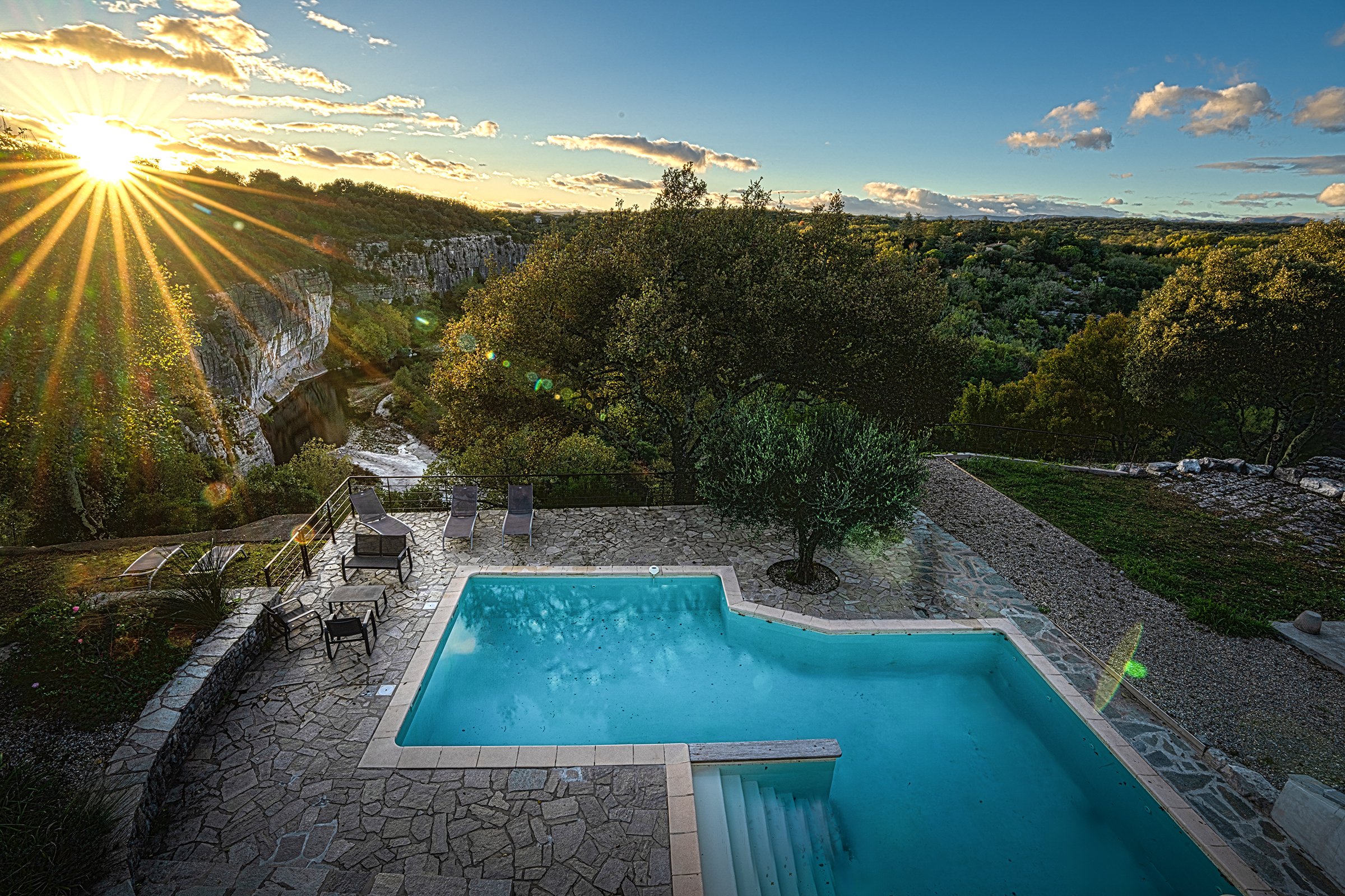 Piscine atypique avec vue panoramique sur la nature, falaises et arbres, rivière Beaume coulant au fond, rayons de soleil, ambiance