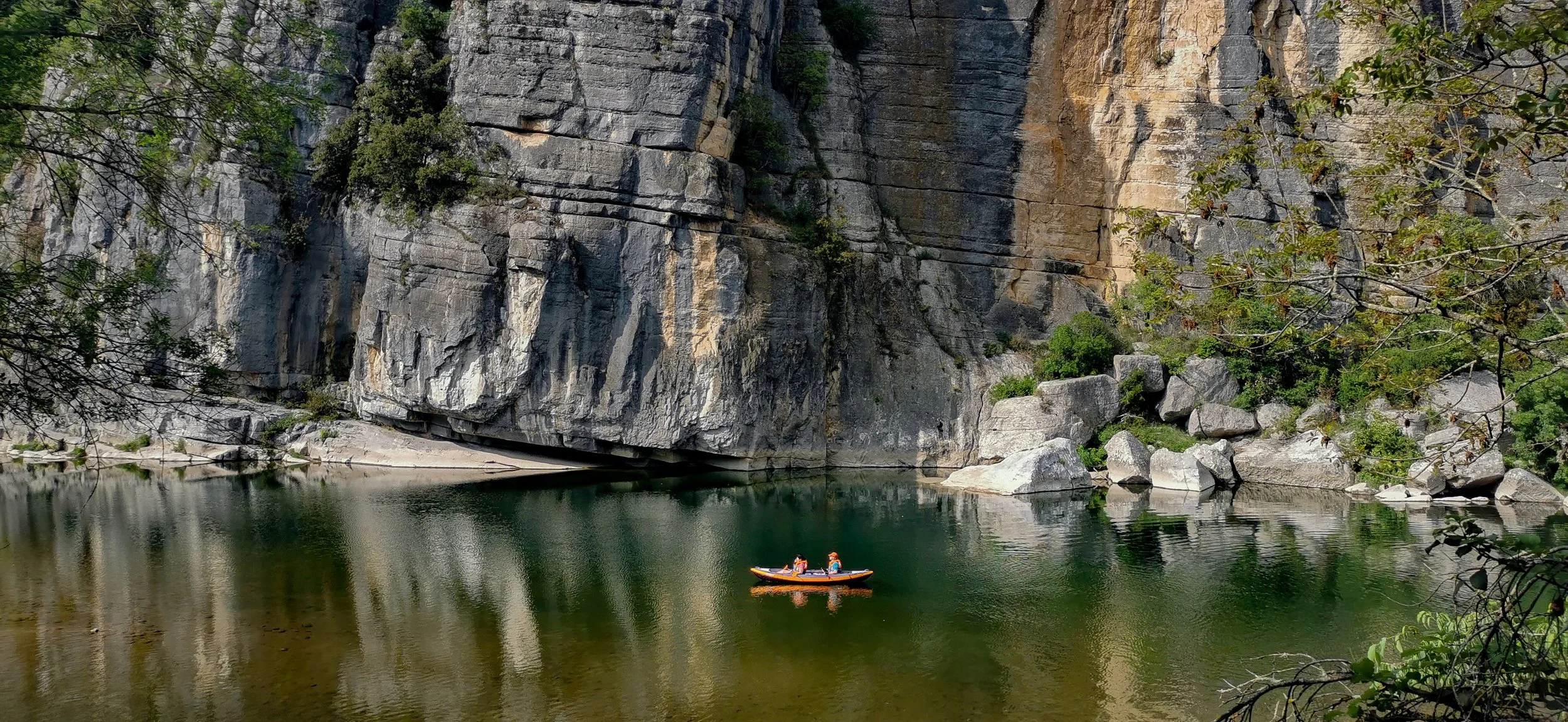 Deux personnes faisant du kayak sur la rivière Beaume, Chauzon, Ardèche, entourée de falaises rocheuses et de feuillage vert.