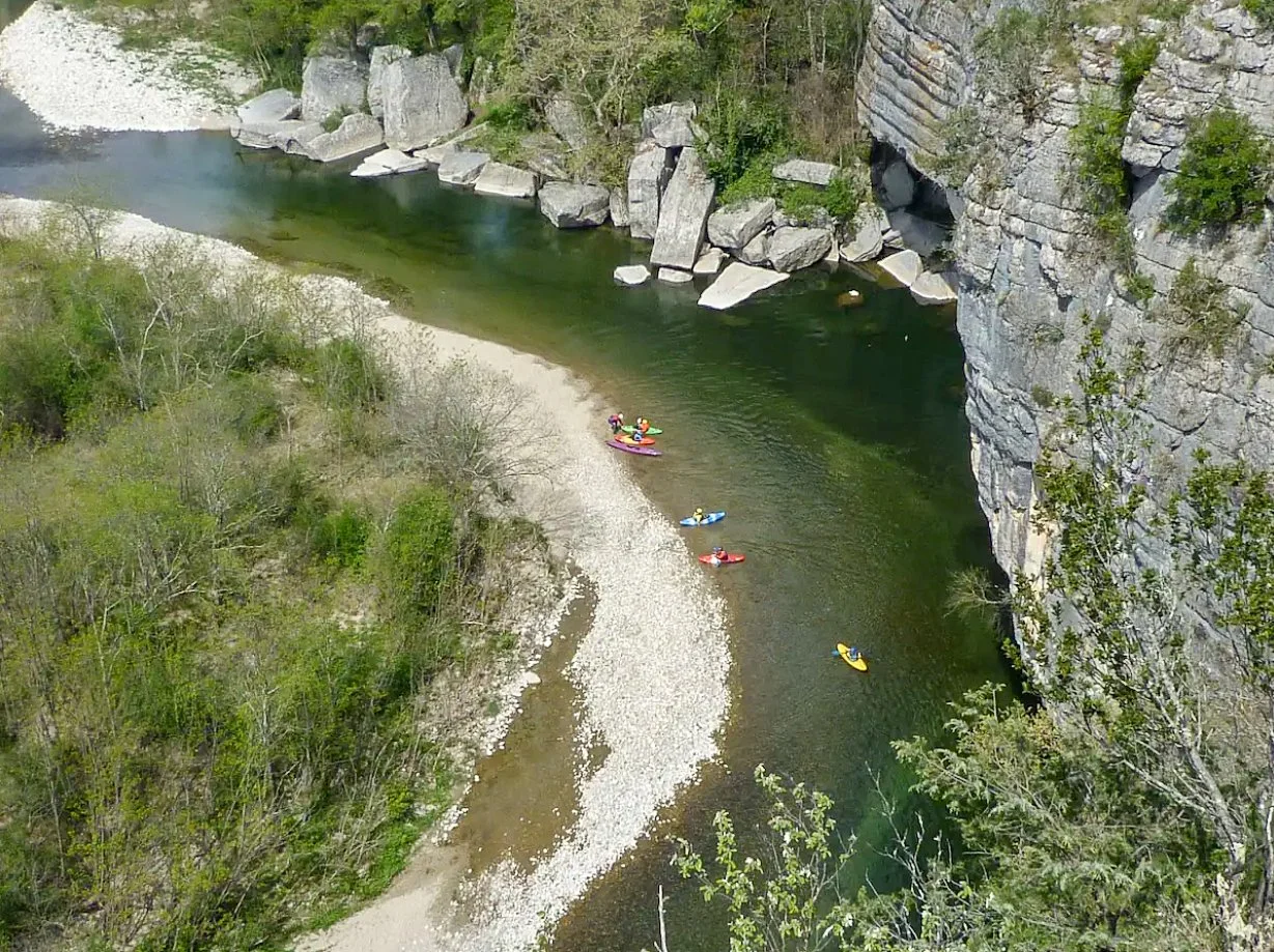Groupe de personnes en kayak et paddle sur la rivière Beaume, plage de la Jarjatte, Ruoms, Ardèche, bordée par des falaises rocheuses et une forêt.